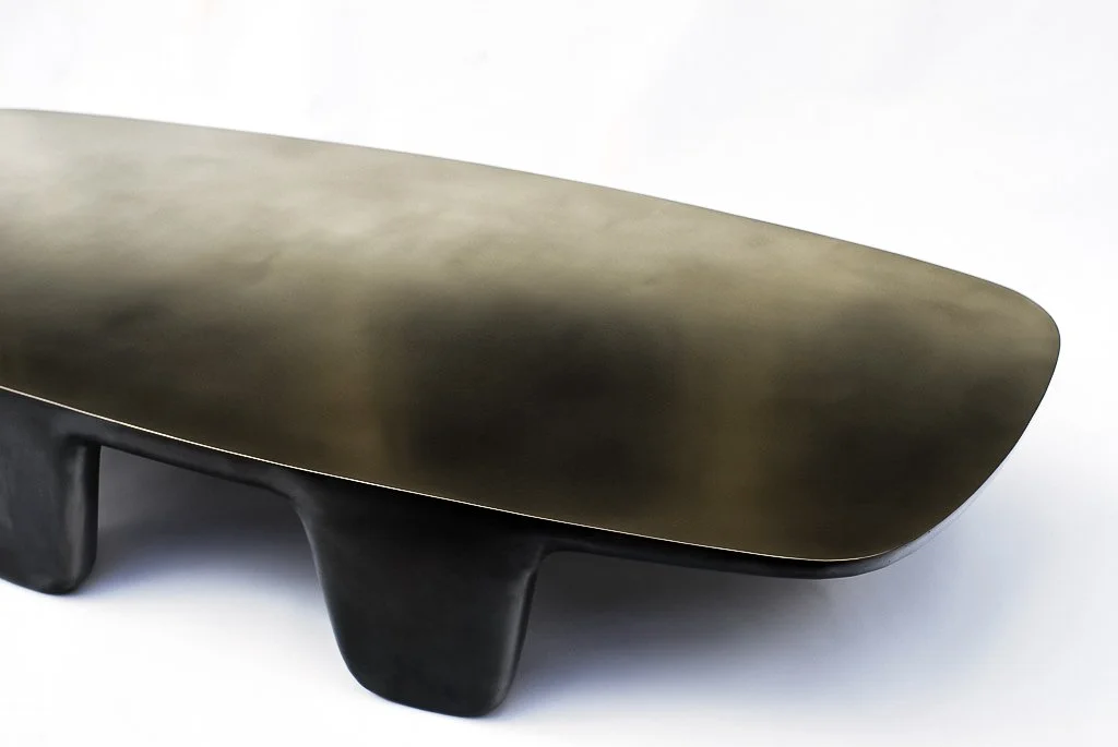 Close-up of a modern minimalist coffee table with a black rectangular top and three curved black legs, against a white background.
