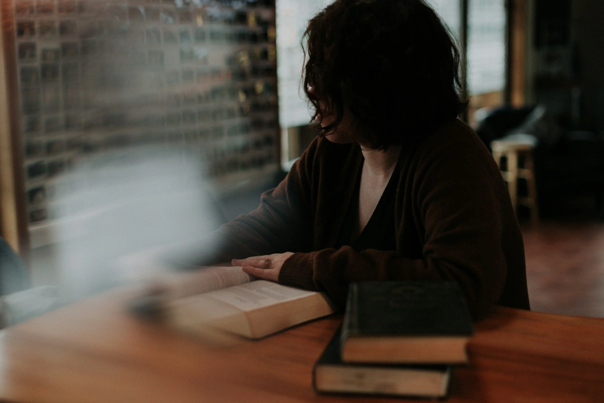 A person with dark, curly hair looking down and working on papers at a desk in a room with large windows.