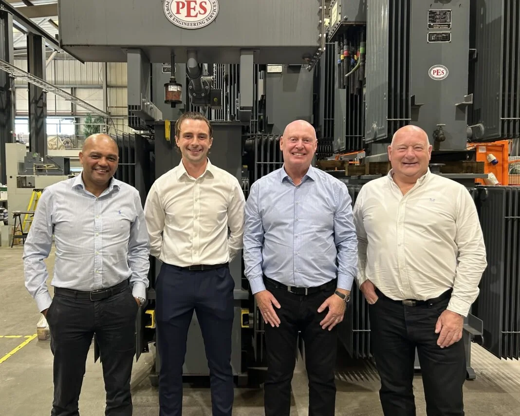 Four members of the Triton Project Solutions and Power Engineering Services leadership team standing in front of transformer equipment at PES facilities