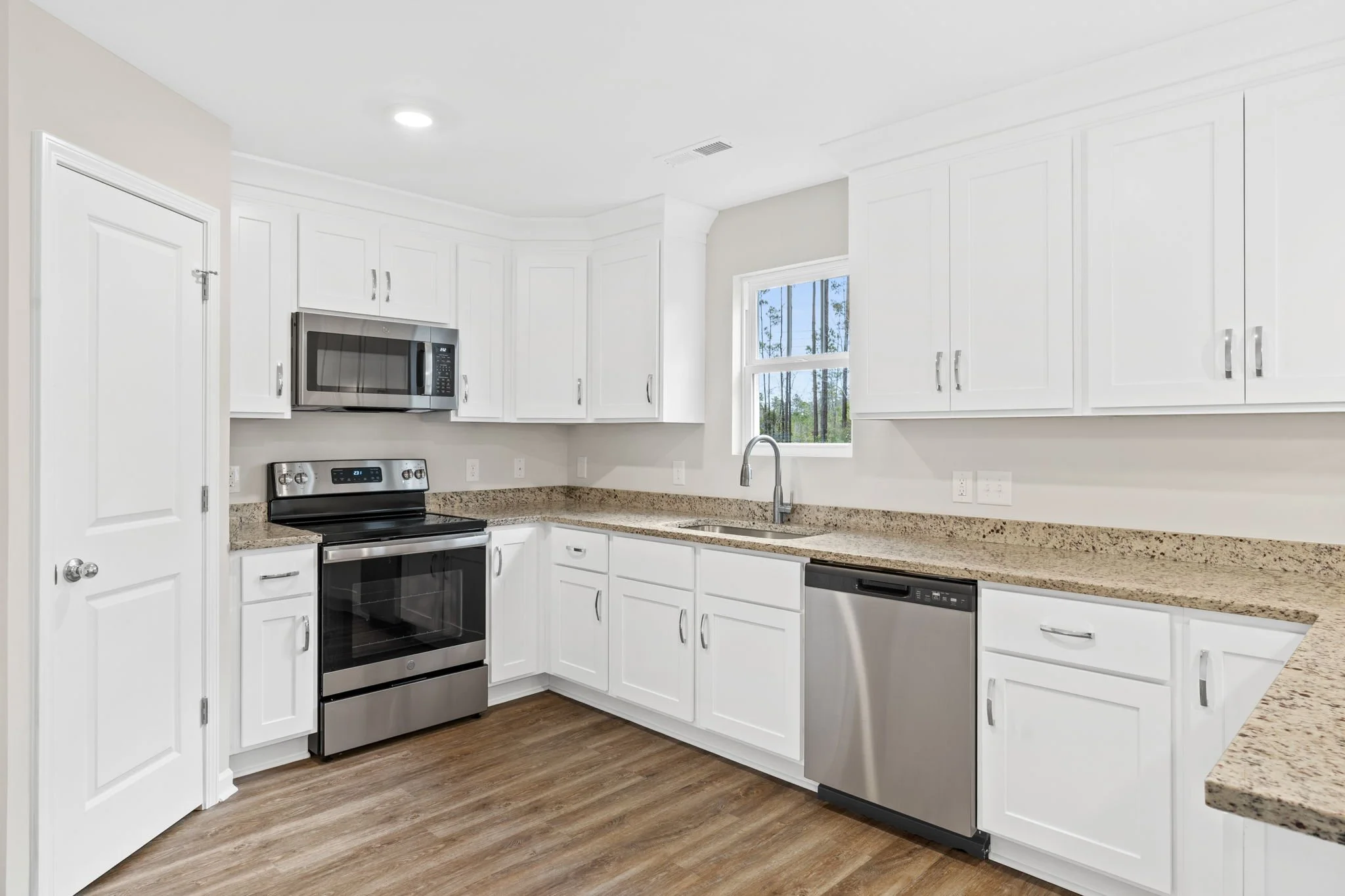 Modern white kitchen with granite countertops, stainless steel appliances, including stove, microwave, and dishwasher, and a window above the sink.