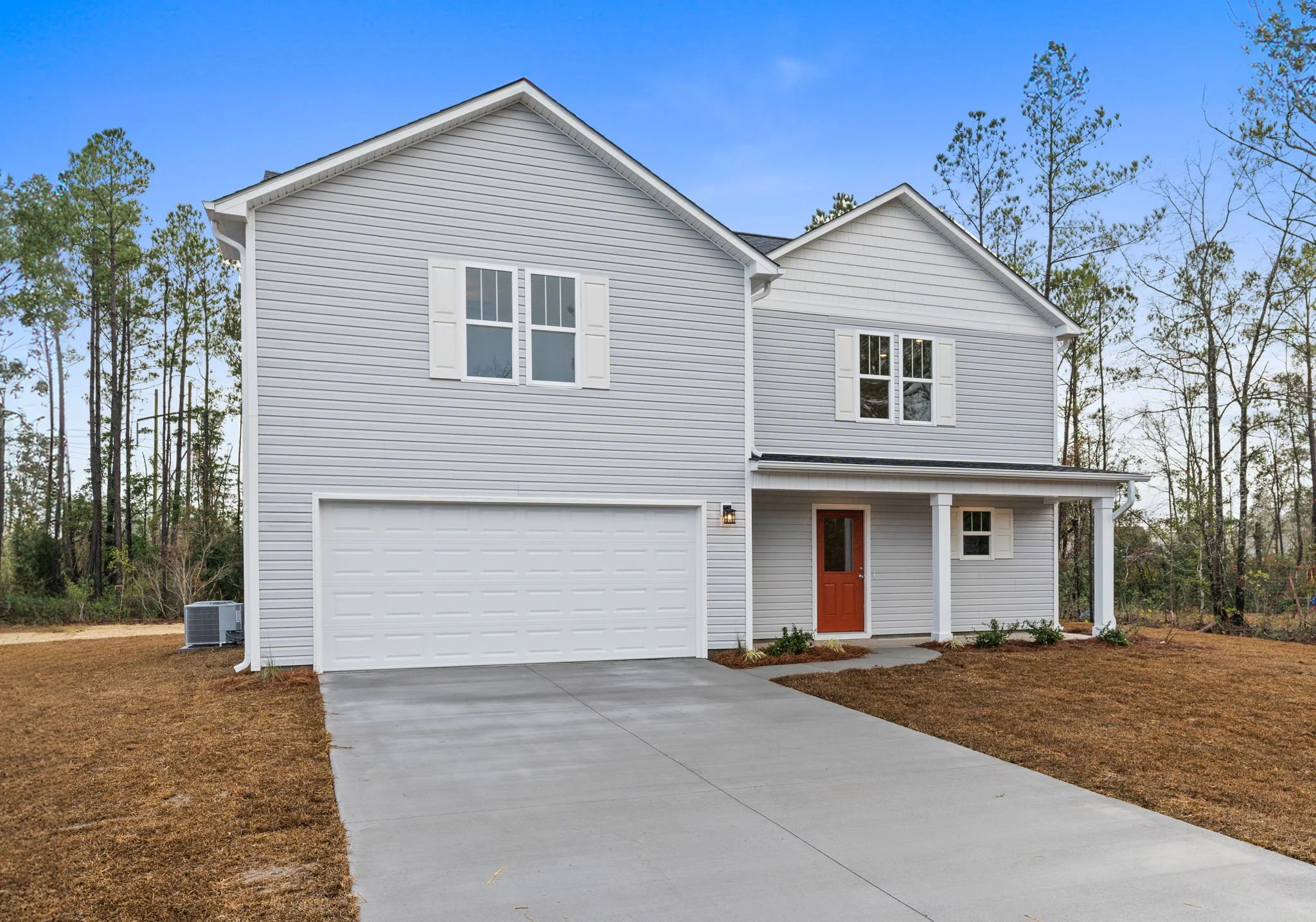Front view of a two-story house with gray siding, white trim, and orange front door, against a blue sky with sparse tree background.