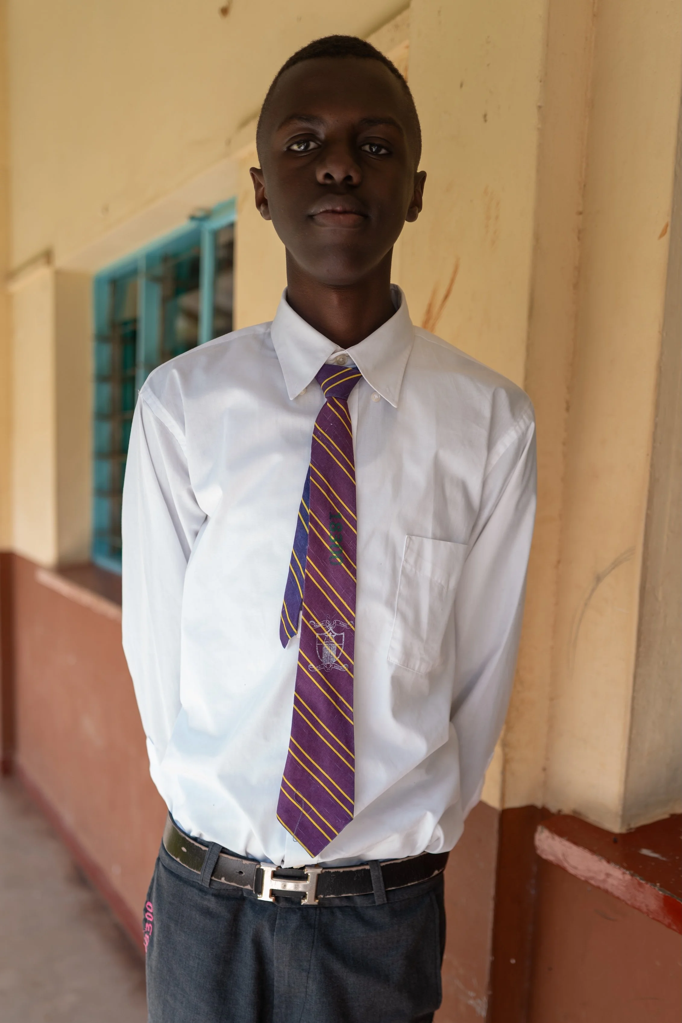 A young boy dressed in a white shirt and striped tie standing in a school hallway.
