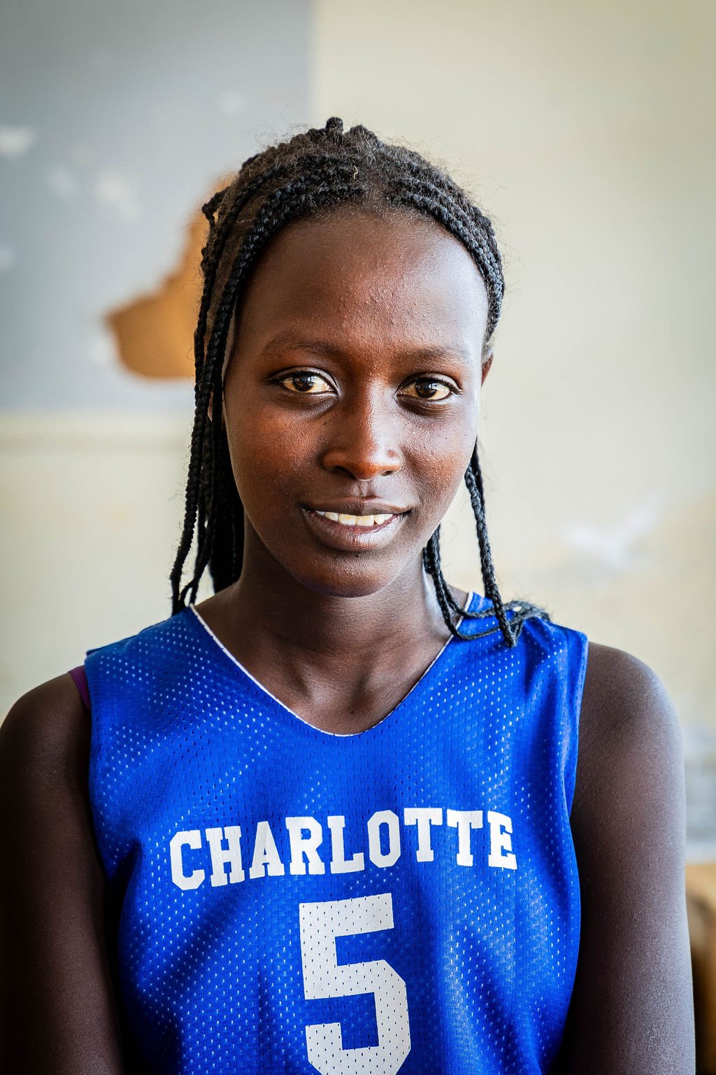 Young woman wearing a blue "Charlotte" basketball jersey with number 5, smiling.