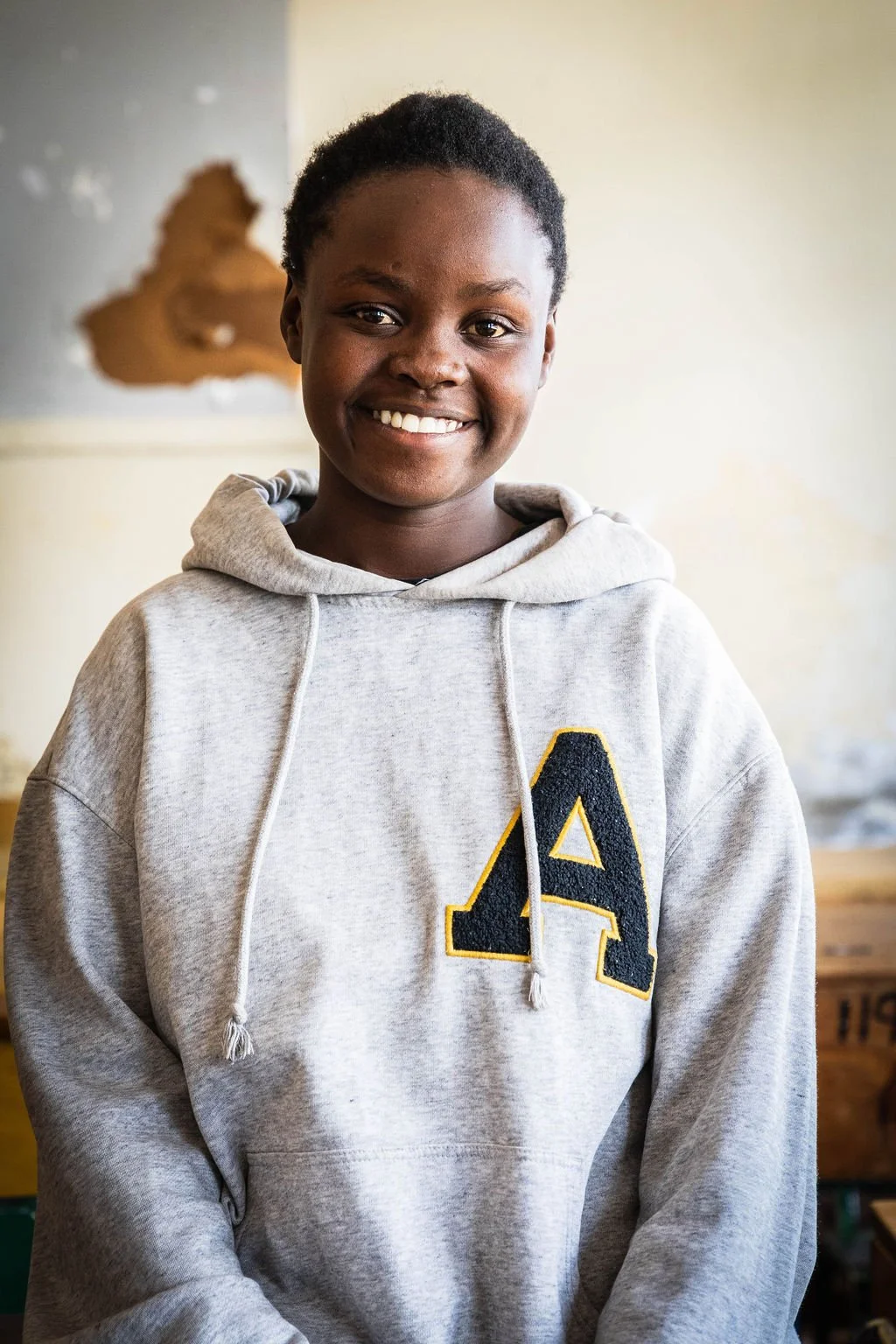 Person wearing a gray hoodie with a large letter 'A', smiling in an indoor setting.