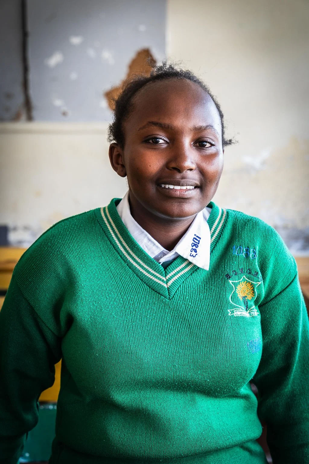 Student in a green school sweater smiling indoors.