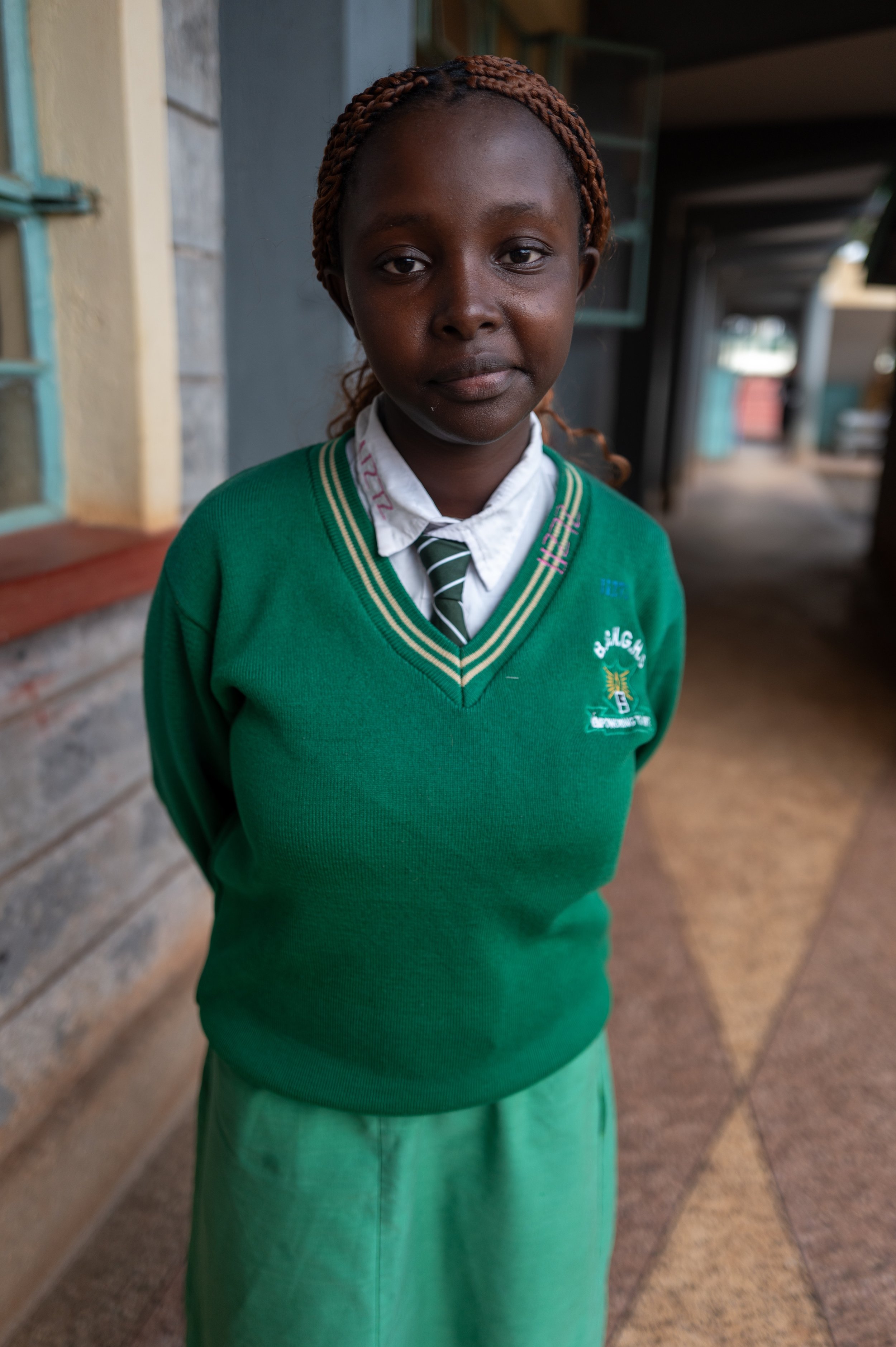 A young girl in school uniform standing in an outdoor corridor.