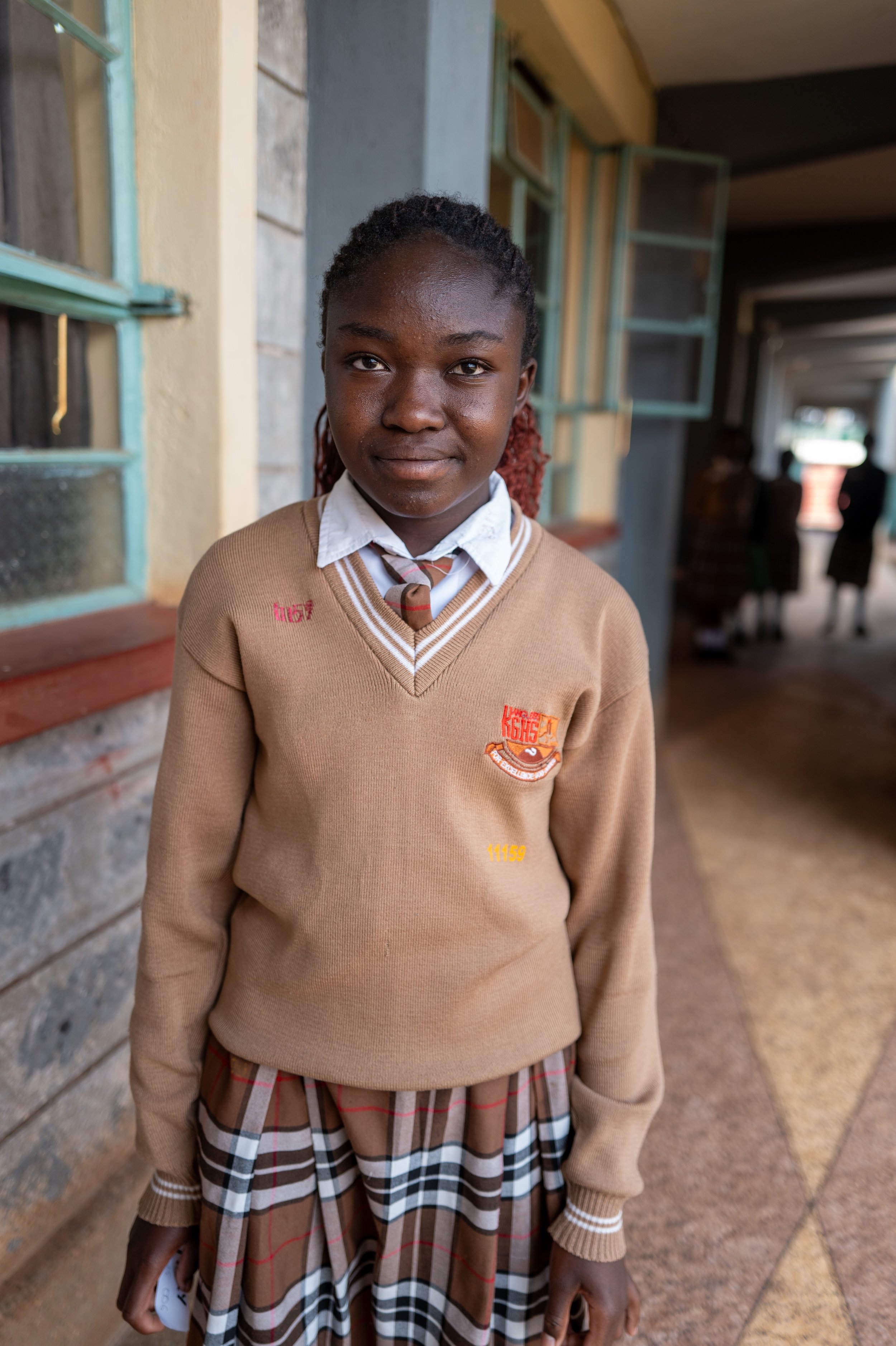 A young girl in school uniform standing in a school hallway.