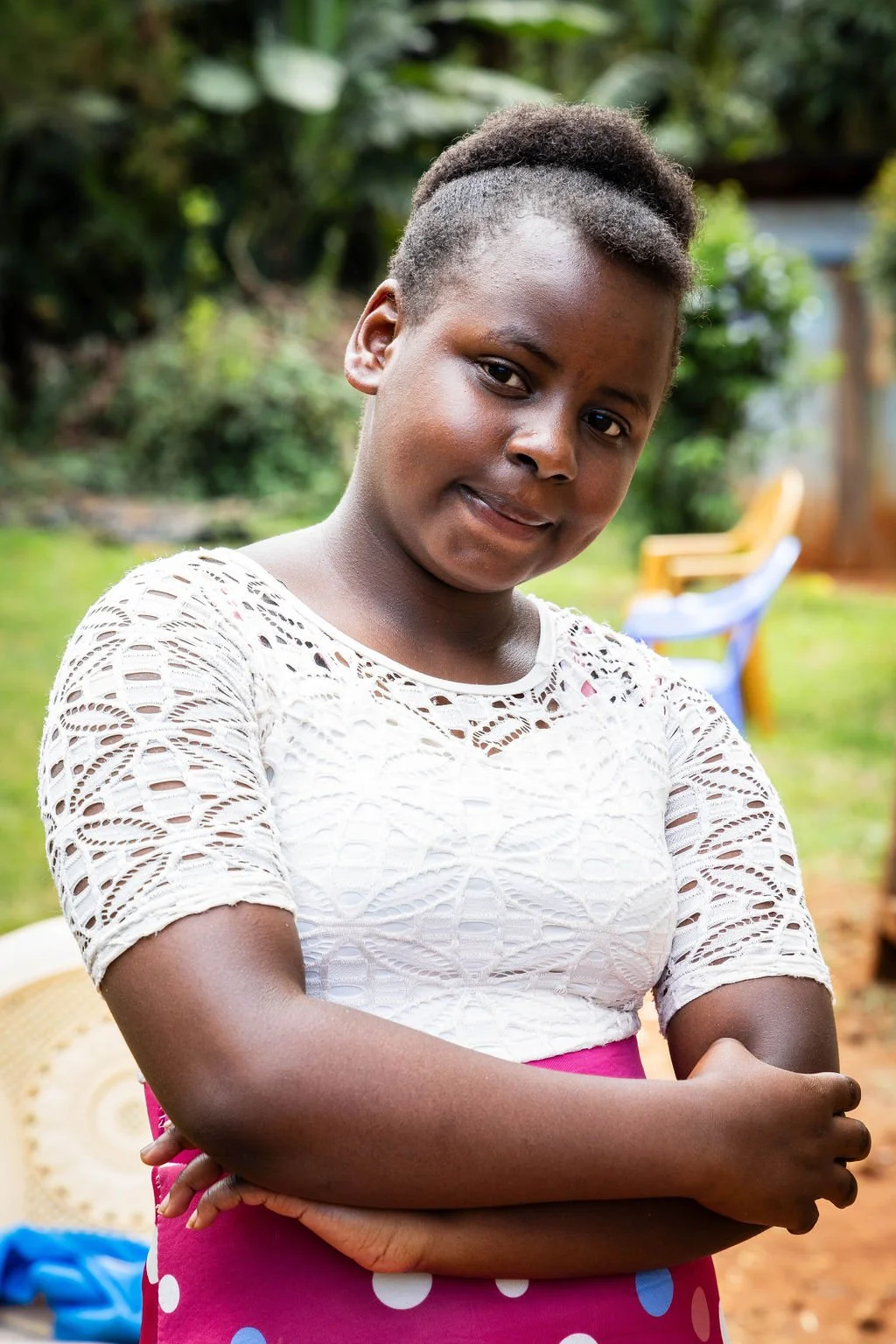 Person in a white lace top and pink polka dot skirt standing outdoors with crossed arms.