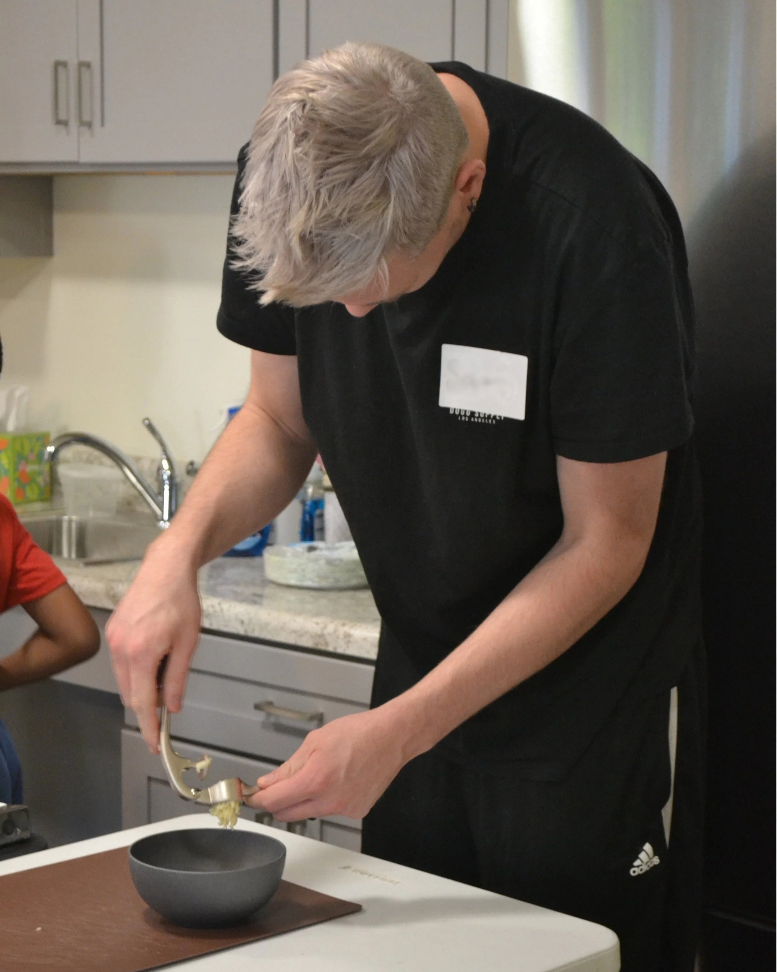Kitchen Compass client using a garlic press to press garlic into a bowl while prepping Caesar salad dressing.