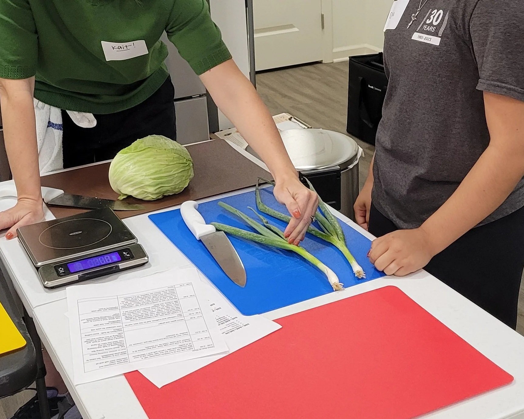 Kait of Burkett Farm showing a Kitchen Compass client where to cut green onion on a cutting board.