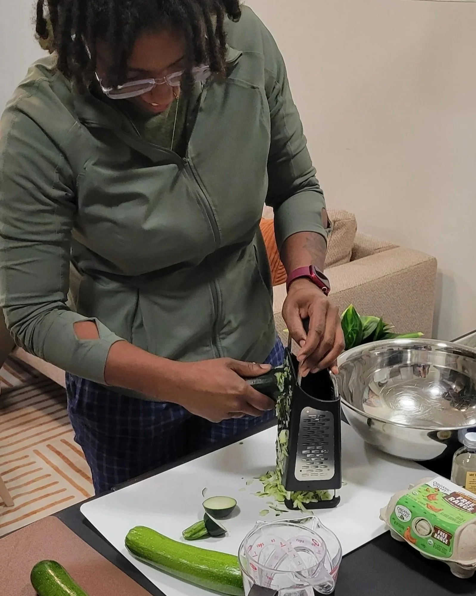 A Kitchen Compass client using a box grater to shred zucchini on a cutting board.