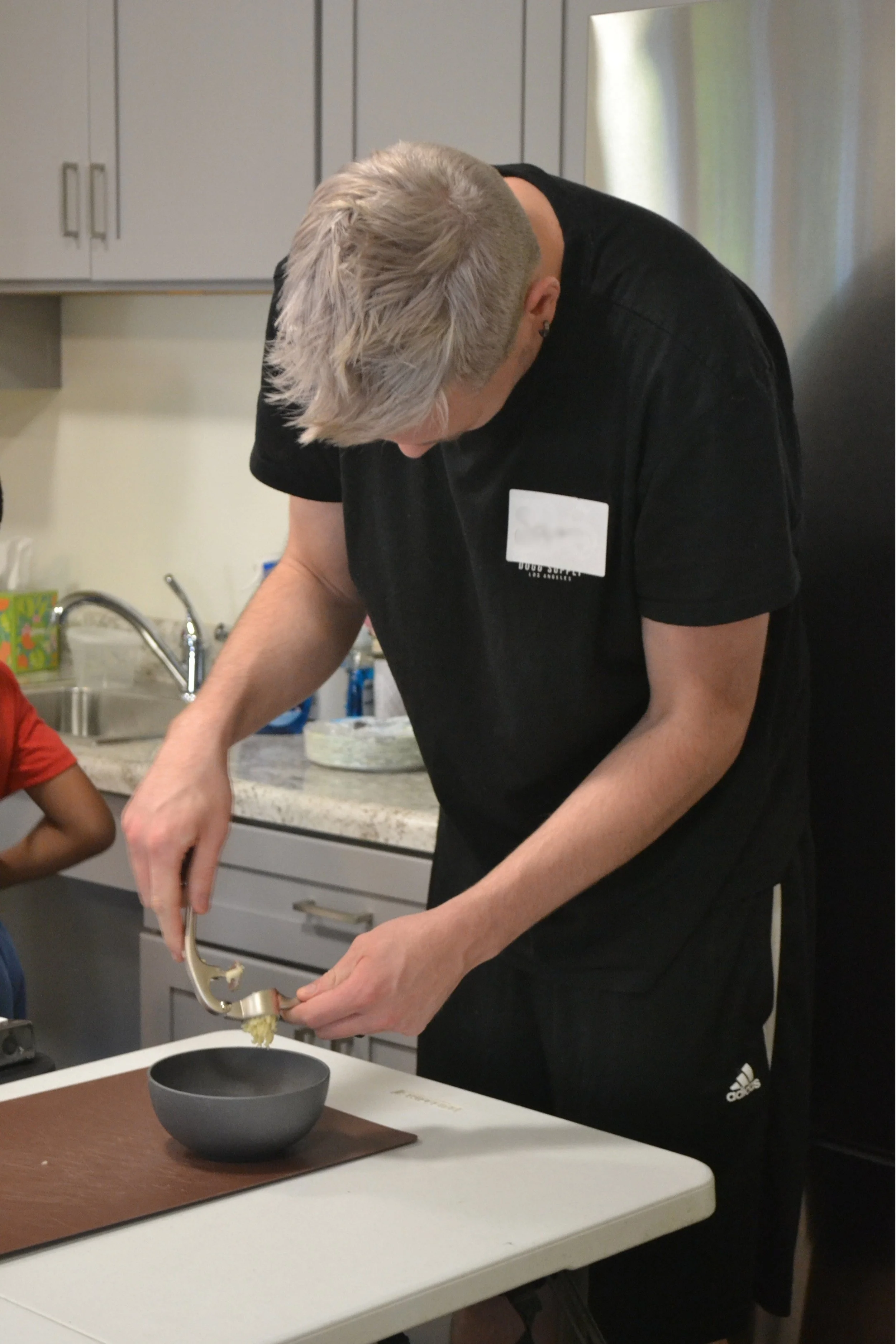Kitchen Compass client using a garlic press to press garlic into a bowl while prepping Caesar salad dressing.