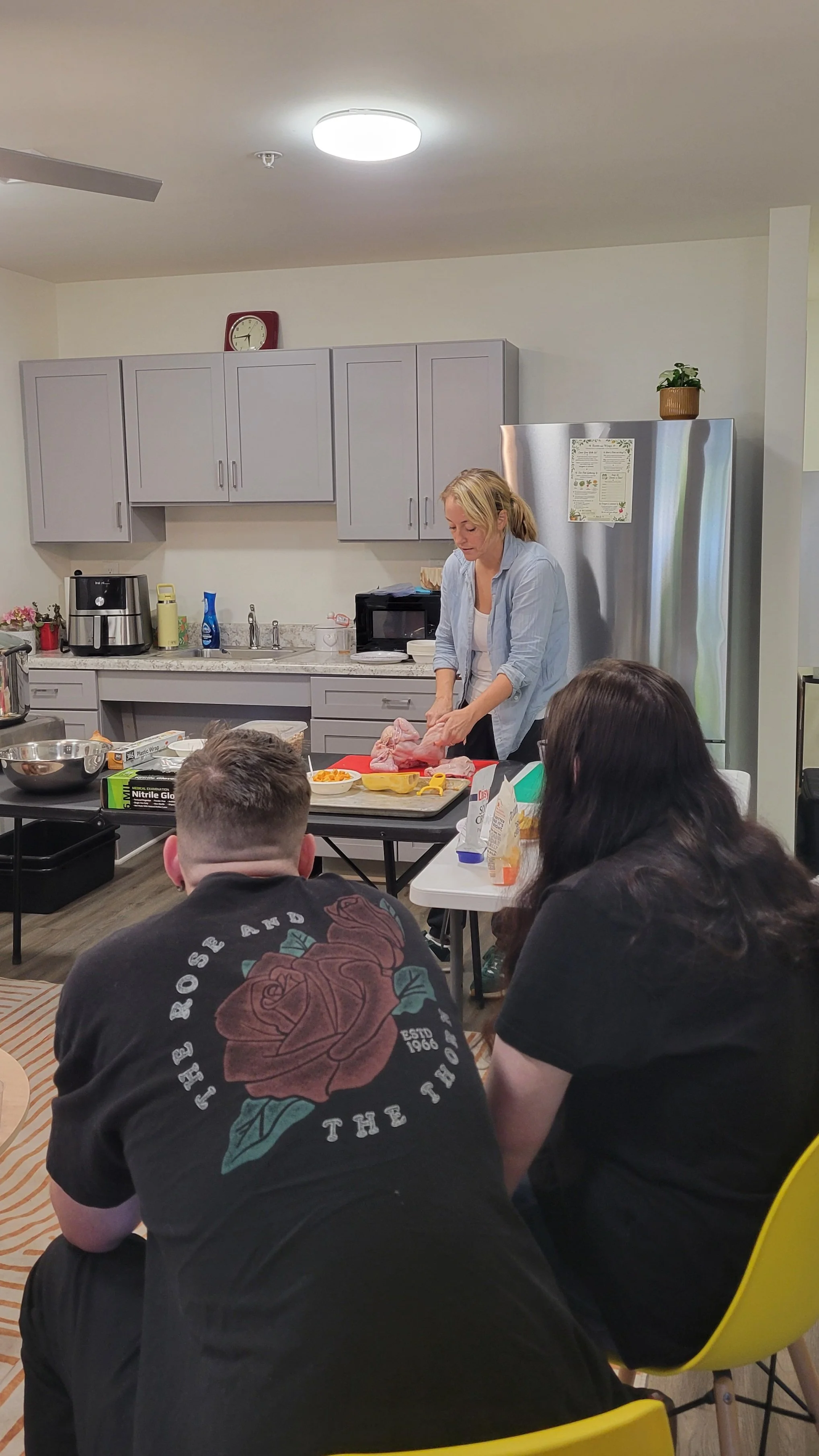 Kait of Burkett Farm deconstructing a whole chicken as Kitchen Compass clients look on.