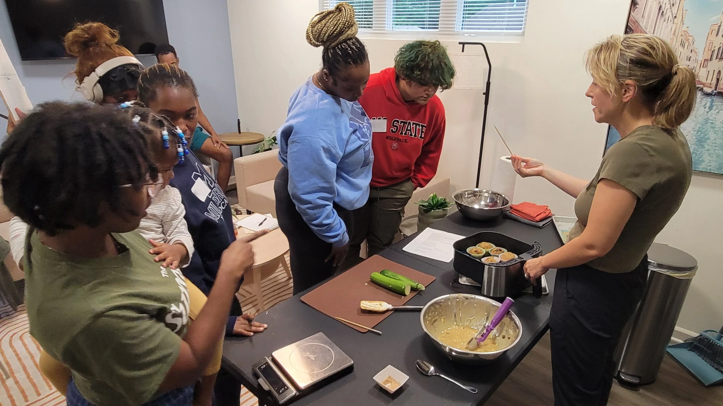 Several Kitchen Clients look on as Kait of Burkett Farm shows them how to use a toothpick to tell if the muffins are fully baked.