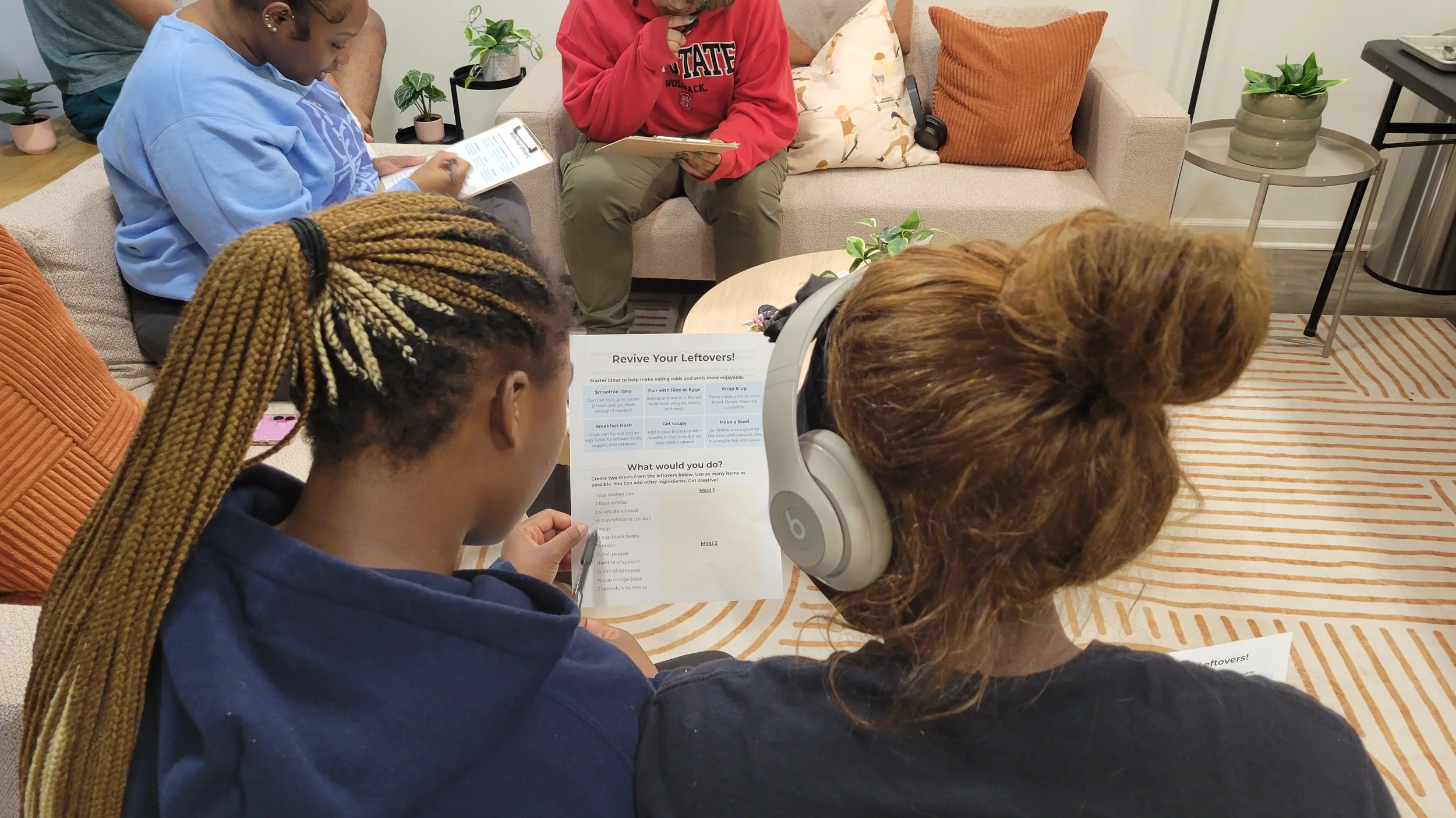 Two women looking at a paper reading a "Revive your leftovers" worksheet with tips and an activity. 