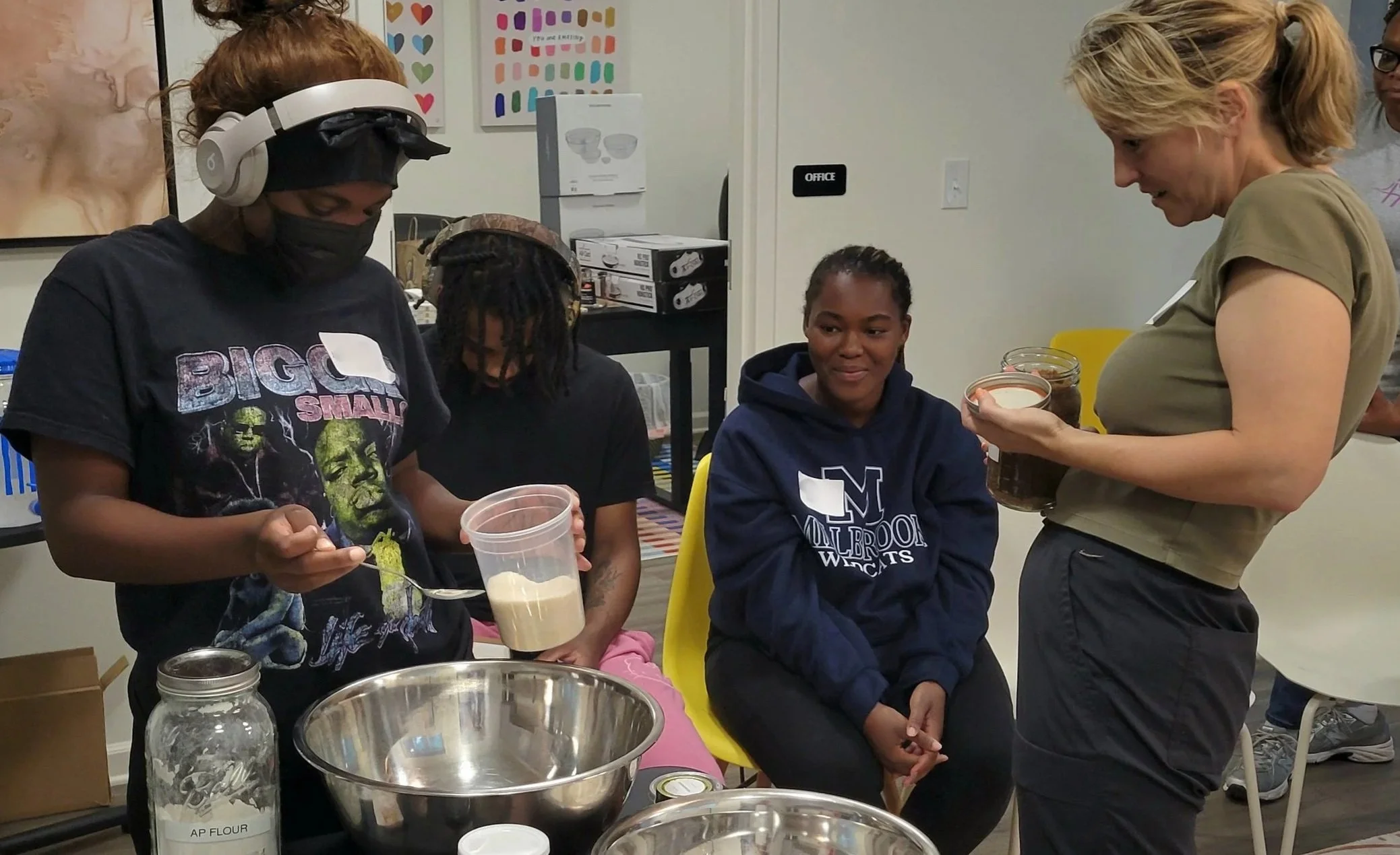 A Kitchen Compass client measuring dry ingredients into a mixing bowl using a scale while others look on.