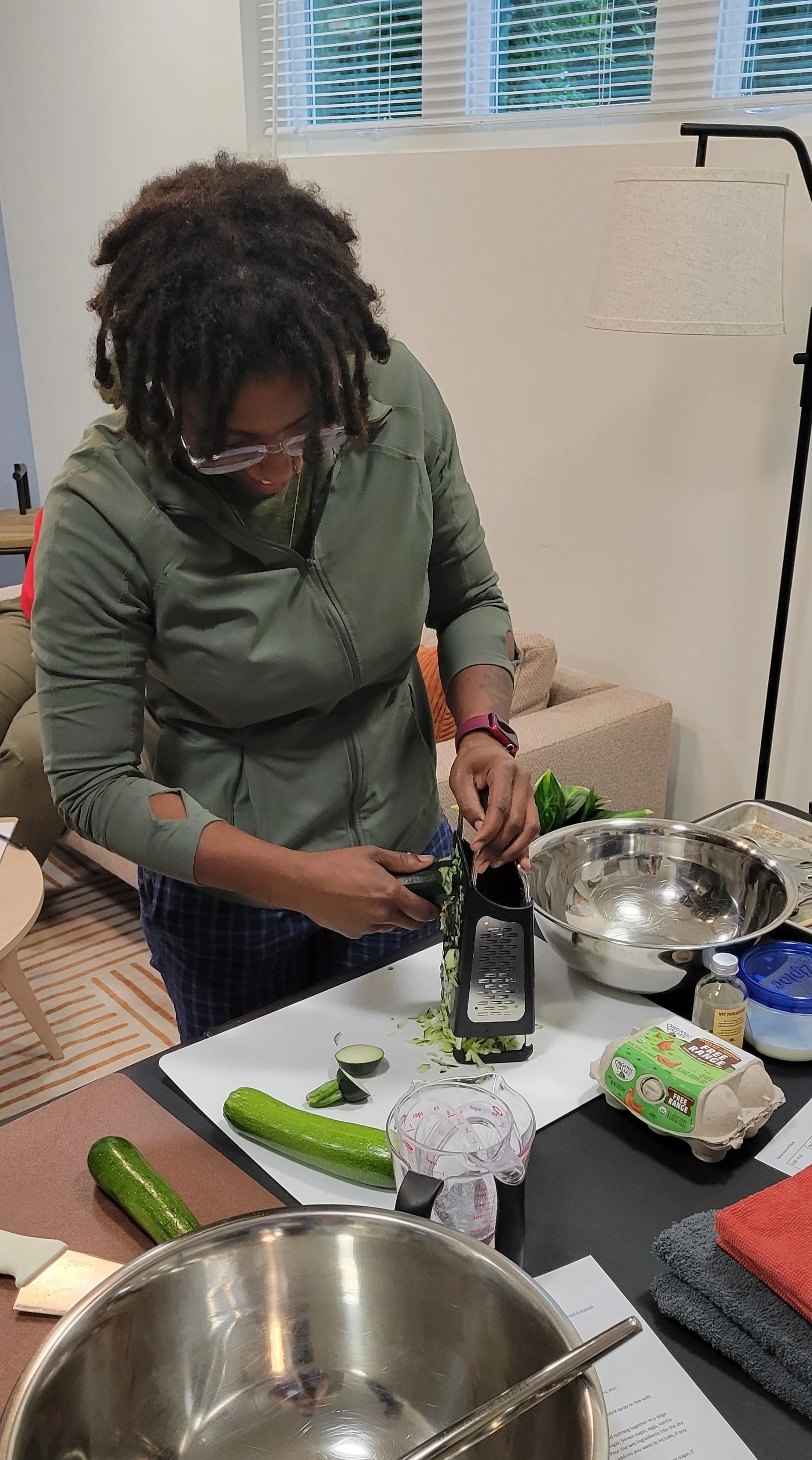 A woman using a box grater to shred zucchini on a cutting board.