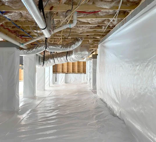 Unfinished basement with exposed ceiling pipes and wiring, covered in white plastic sheeting on floor and walls for construction or renovation.
