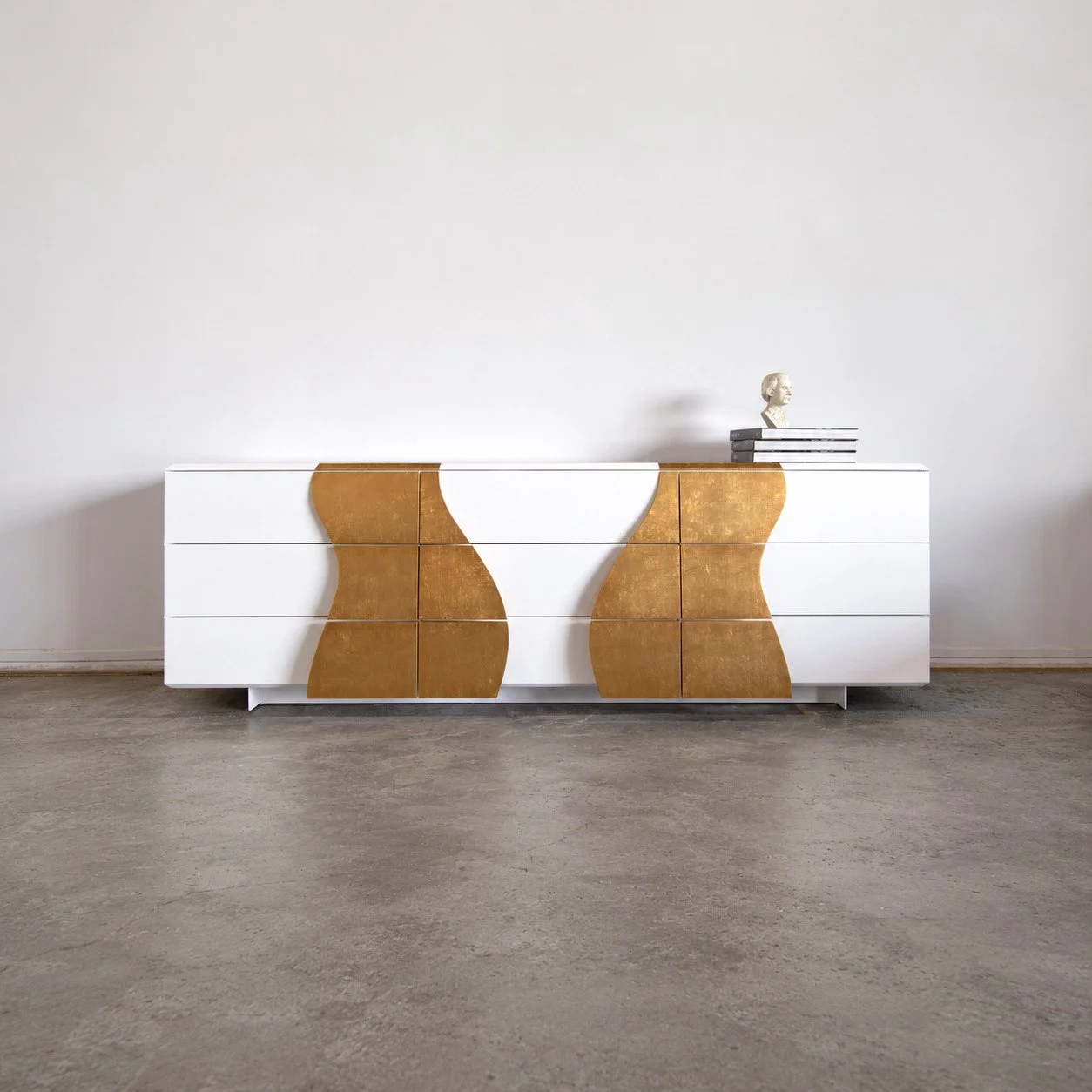 Melodious Dresser against a white wall with books and a bust