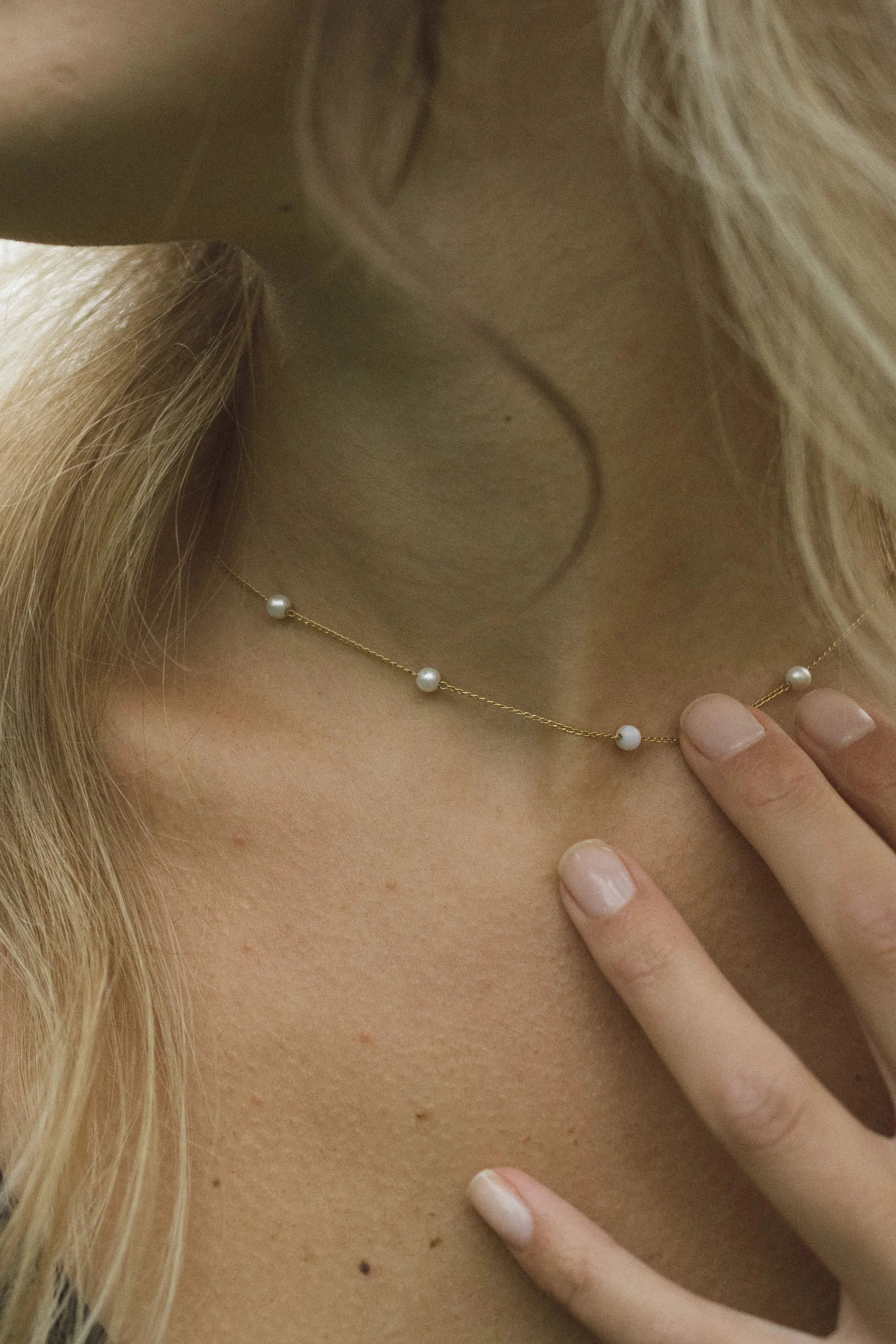 Close-up of a woman wearing a delicate gold necklace with small white pearl beads, resting on her collarbone. Minimalist pearl jewelry styled with a natural, elegant look, perfect for everyday wear or bridal accessories.
Artistic jewelry photography 