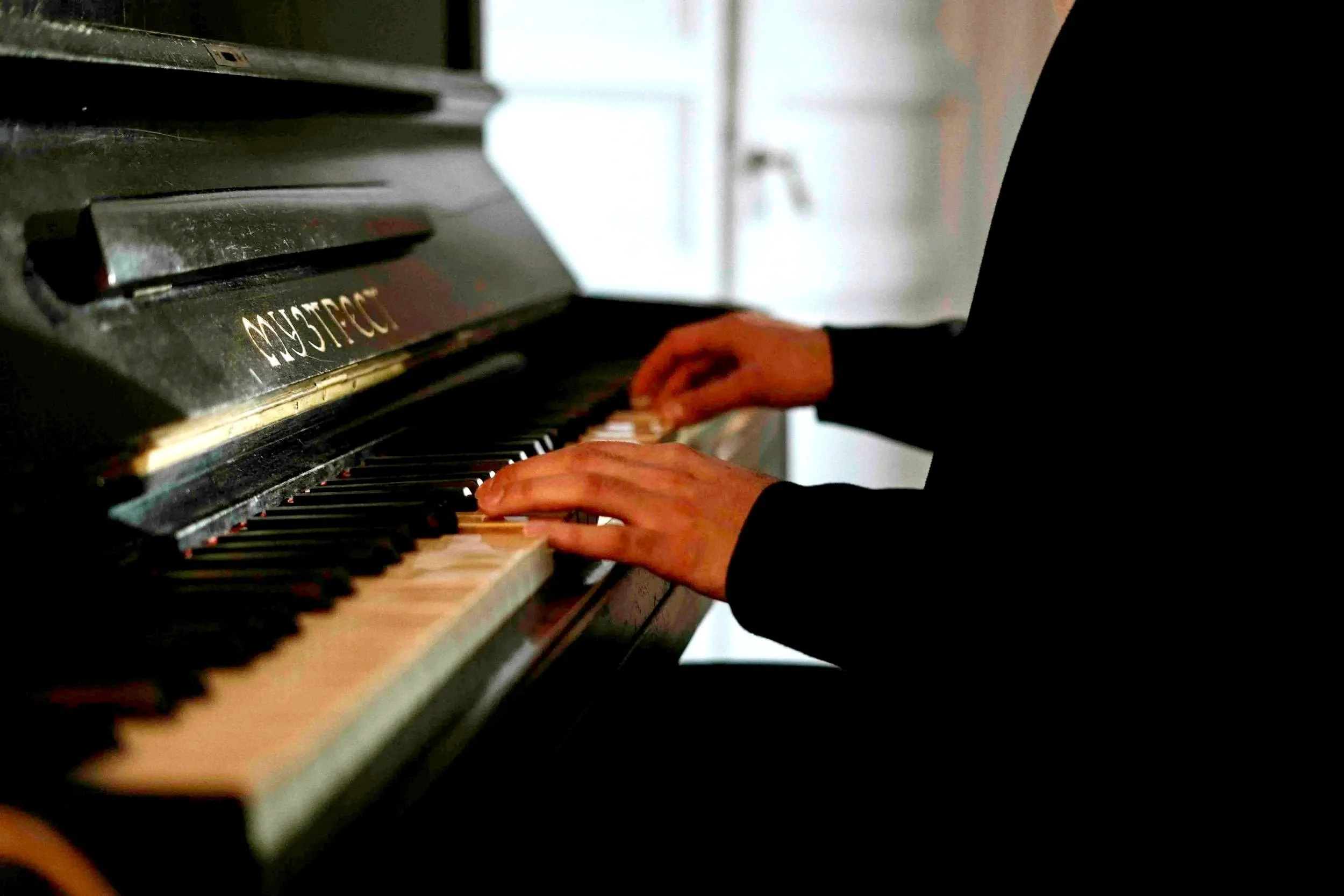 Person playing a black acoustic piano, focusing on hands on the keyboard.