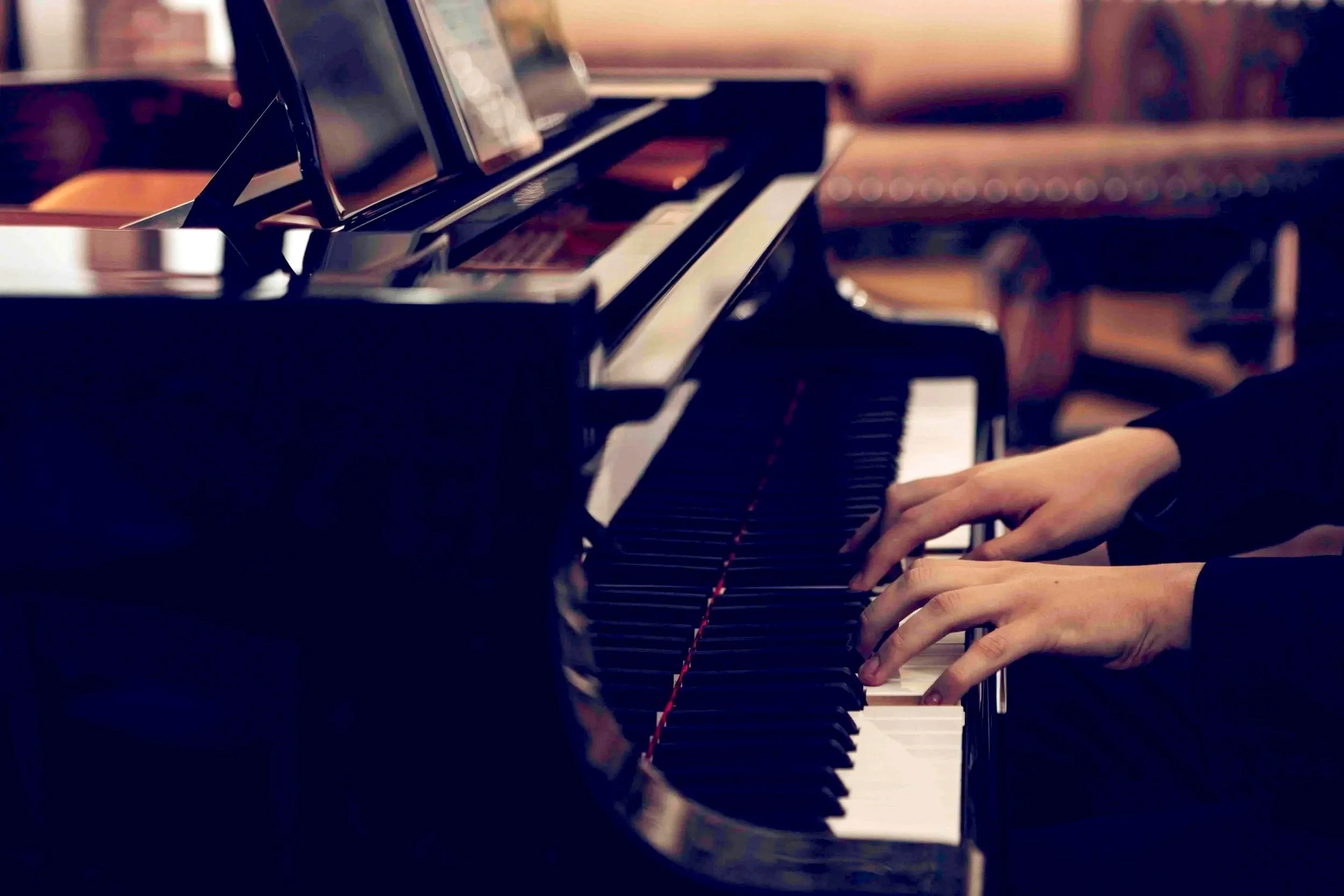 Close-up of a person's hands playing a grand piano in a dimly lit room.