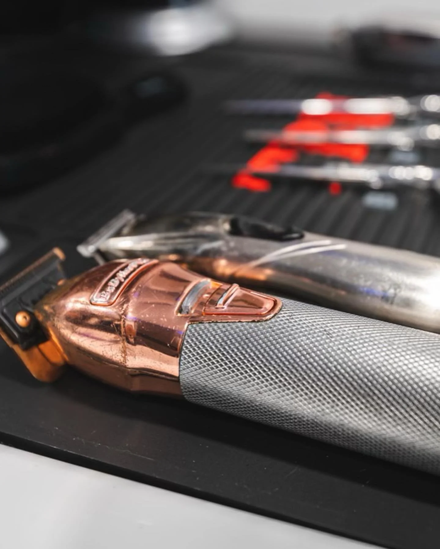 Close-up of a copper-colored safety razor with a textured grip, lying on a black surface with various tools and objects in the background.