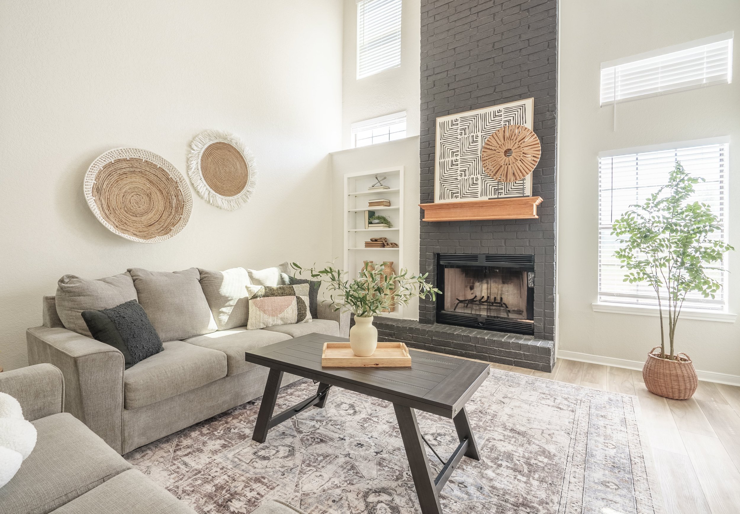 Modern living room with gray sofas, black brick fireplace, decorative wall art, wooden coffee table, and a potted plant.