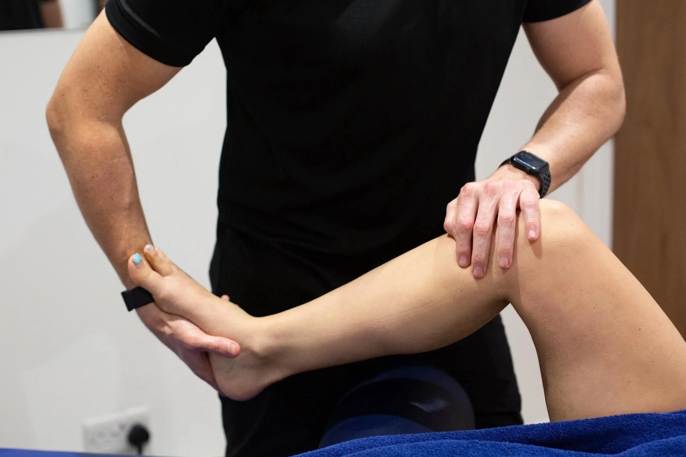 Physiotherapist performing a knee therapy or examination on a patient's leg in a clinic setting.