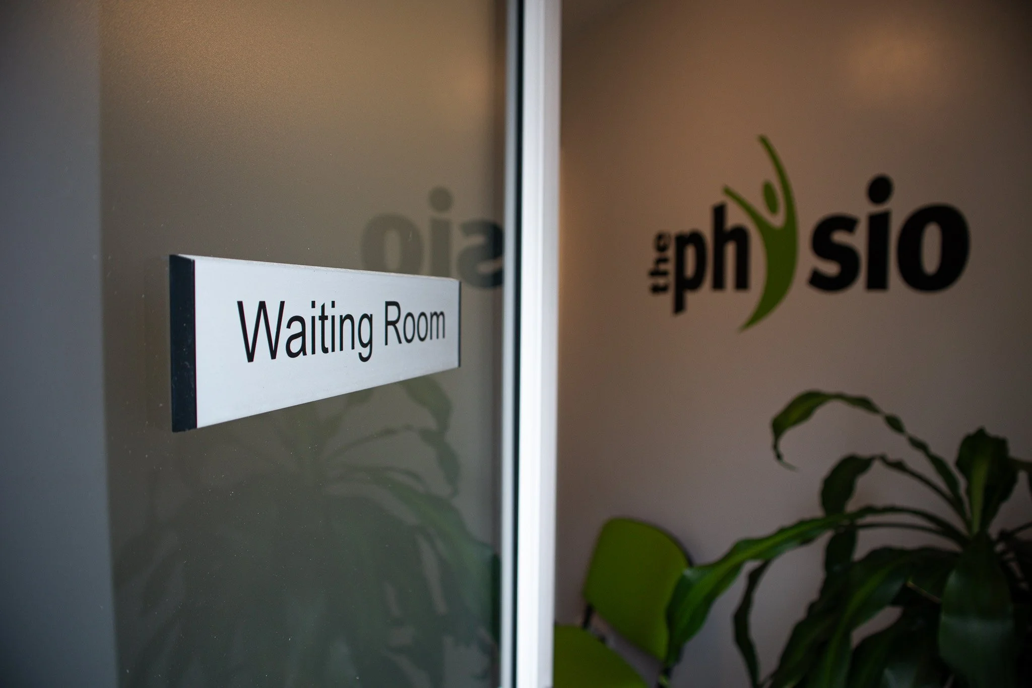 A door with a sign that reads 'Waiting Room' and a room interior with a logo on the wall that says 'the physio' with a green abstract human figure, and some green plants inside.