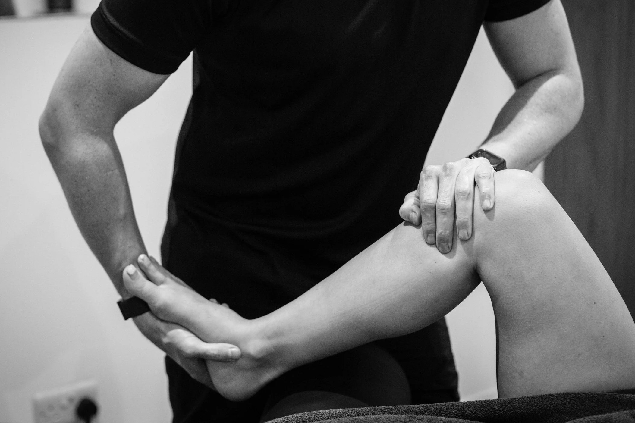 A person wearing a black shirt giving a physical therapy or massage to a patient's leg, which is bent at the knee.