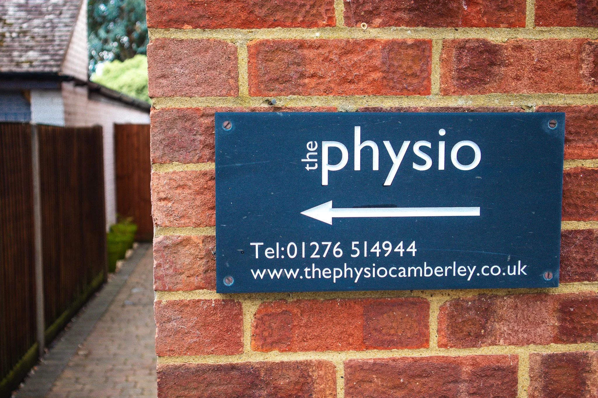 Sign on brick wall pointing left for the physiotherapy clinic, with contact number and website.