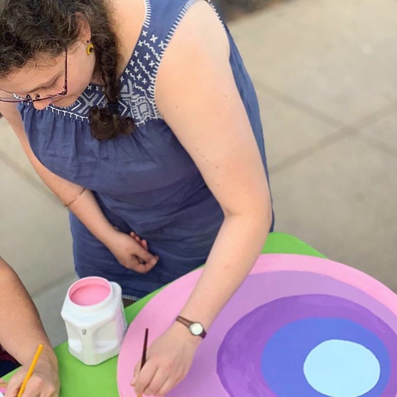 Person painting colorful concentric circles on a round canvas outdoors.