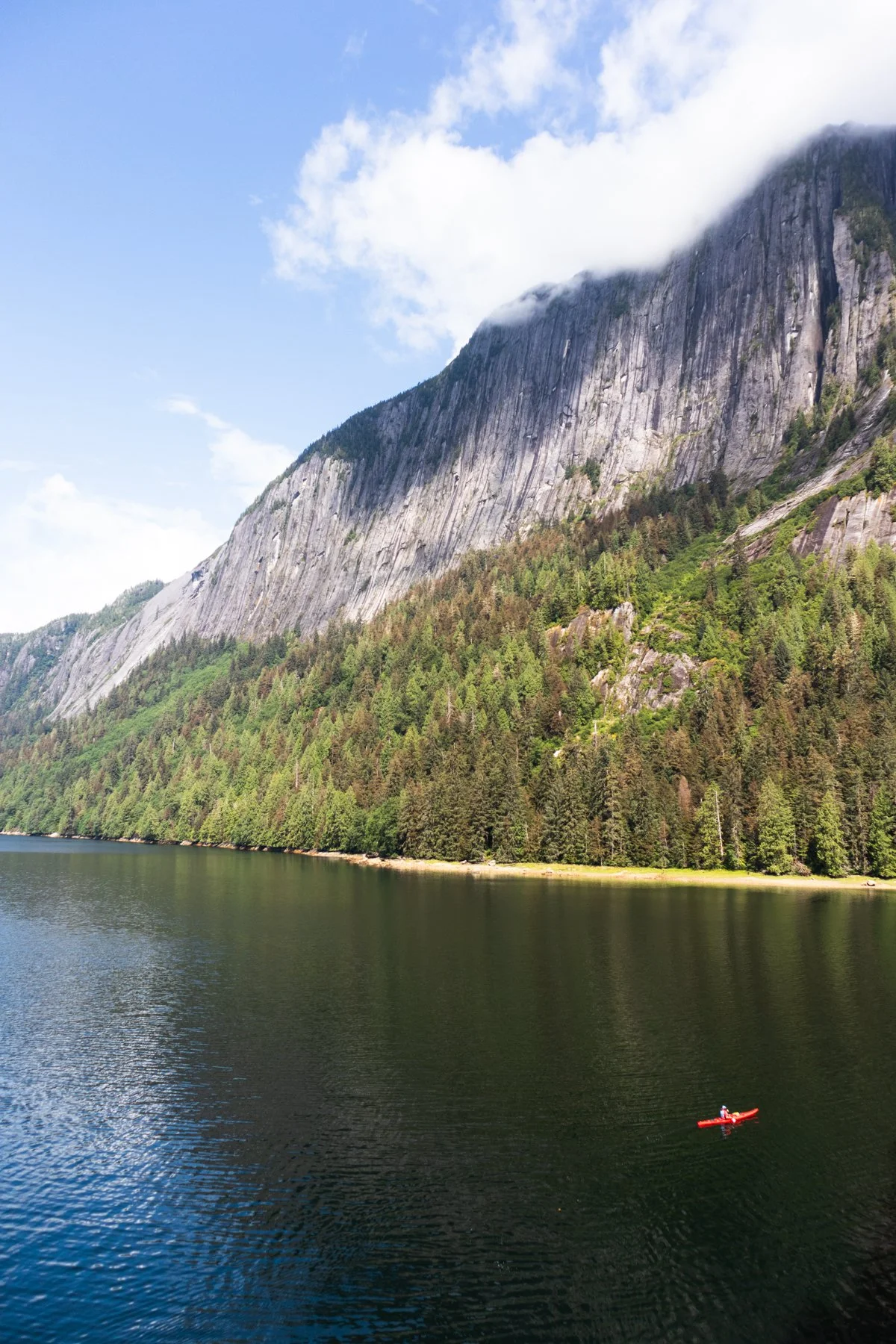 A lone paddler in a red kayak under steep cliffs in Alaska