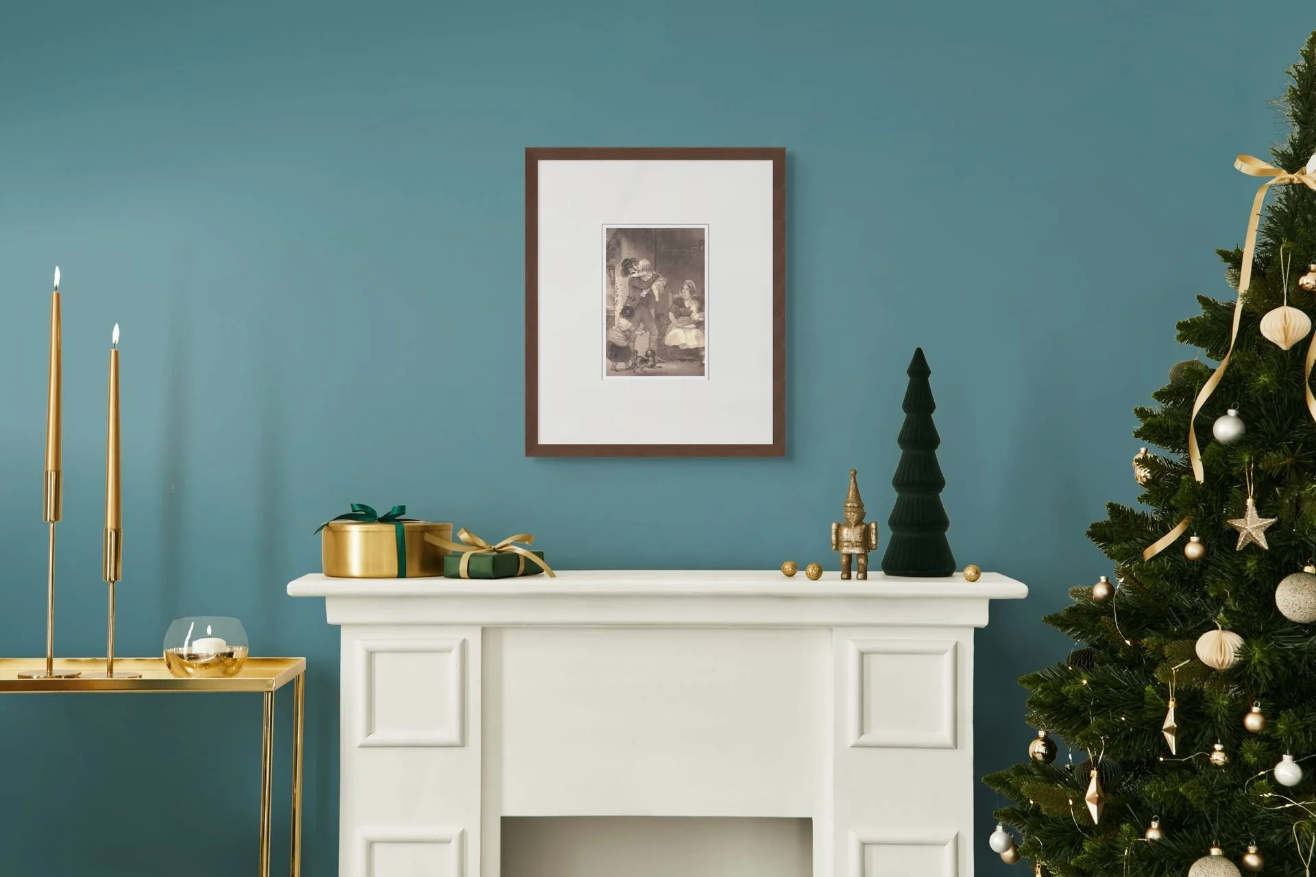 A decorated Christmas tree with gold and white ornaments next to a white fireplace mantel with Christmas presents and holiday decorations on it, and a framed picture on a teal wall.