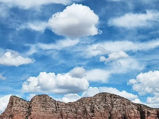 A blue sky with scattered white clouds above rocky mountains.