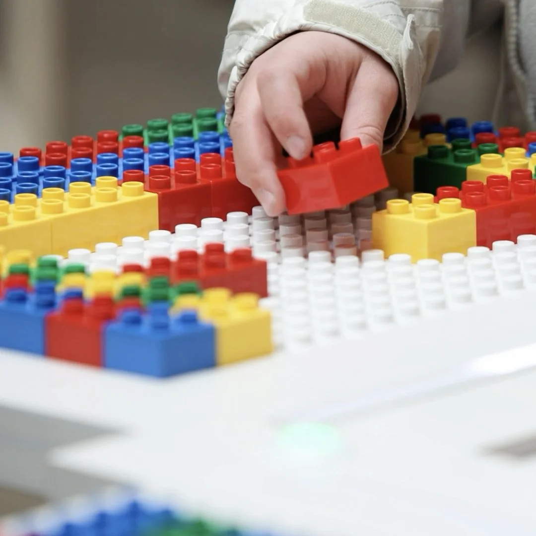 Hand placing a red duplo brick on a baseplate with other coloured bricks