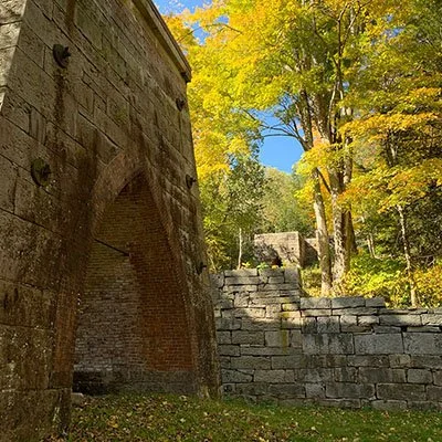 Ruinas históricas de piedra entre los árboles otoñales, un escenario emblemático para los clientes con lesiones personales en Mine Hill, Nueva Jersey