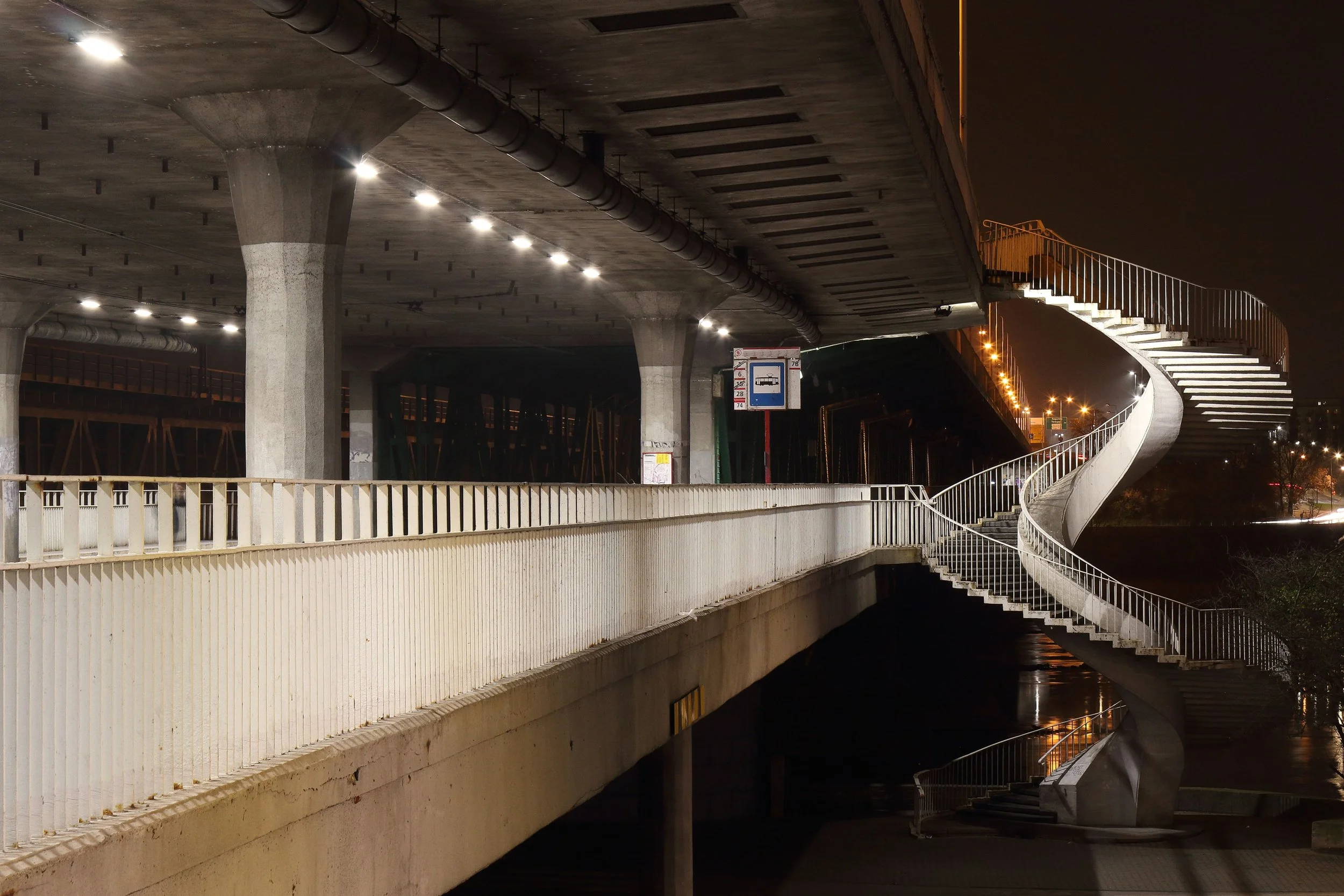Elevated walkway with railing and spiral staircase at night, where ramp and walkway failures can cause injuries