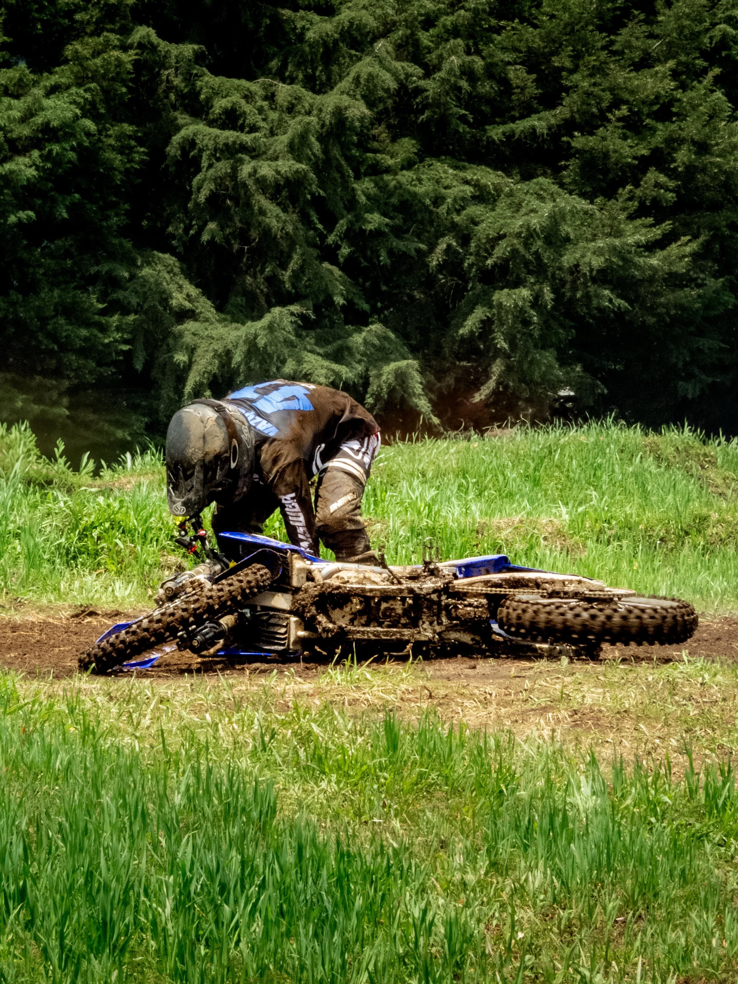 Motorcycle rider kneeling beside a fallen dirt bike after a crash, illustrating insurance bias against motorcyclists