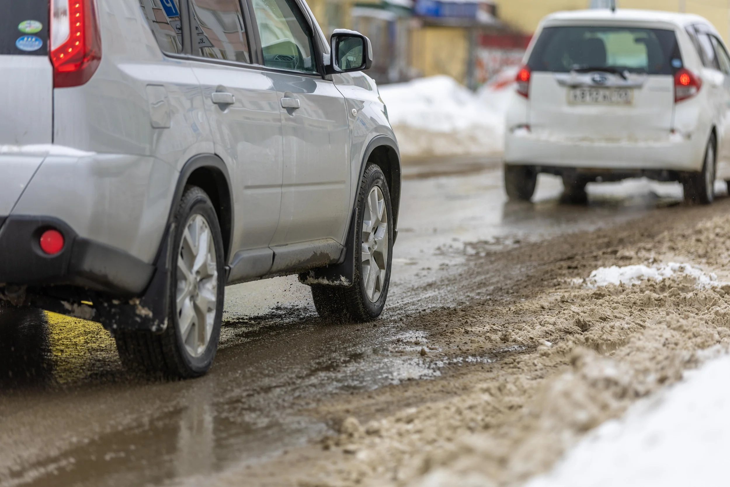 Cars driving on a muddy, snowy road, showing hazardous roadway conditions that can cause bicycle accidents