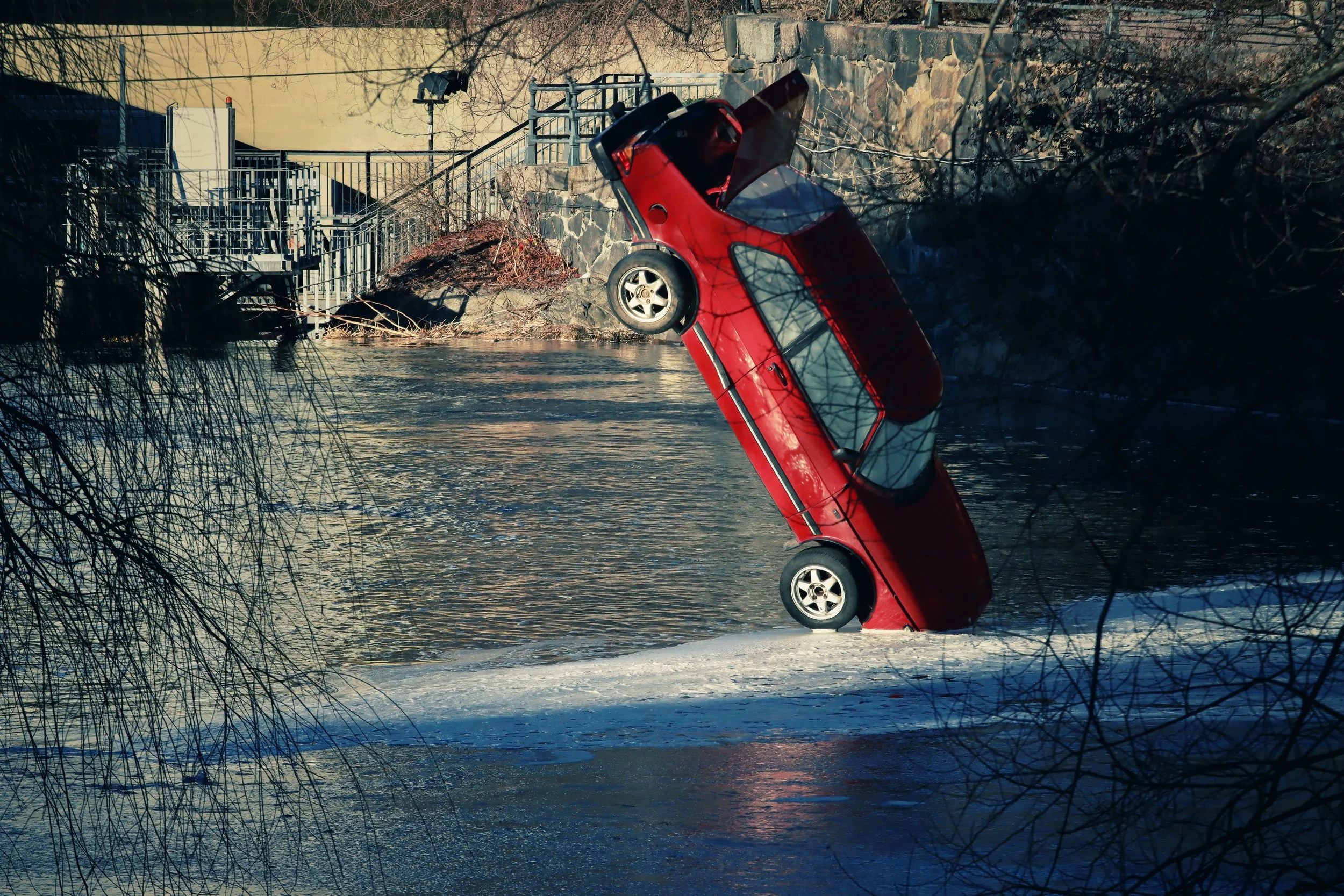 Red car partly submerged nose-down in a river, a severe vehicle collision scenario in a car accident claim