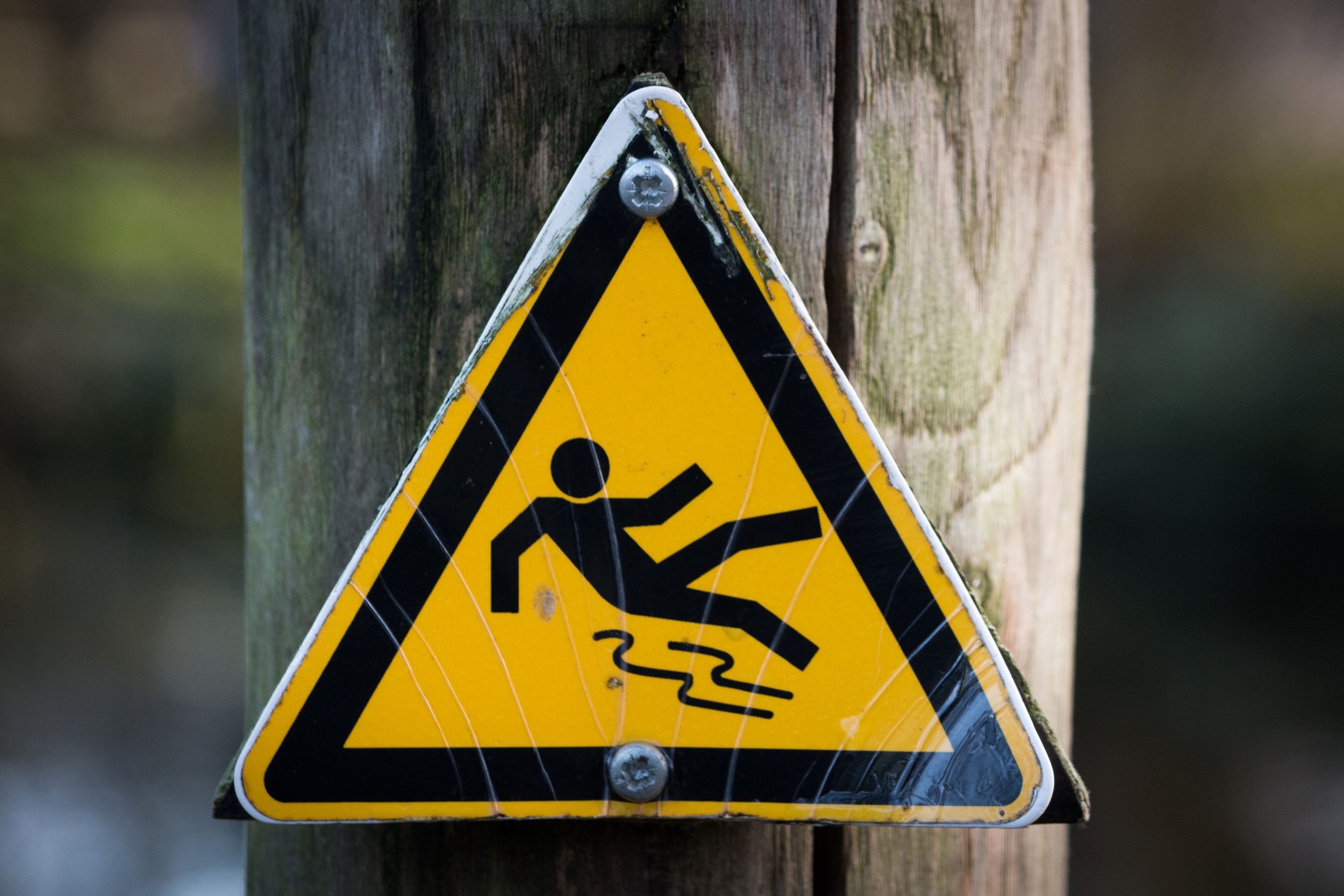 Yellow triangular slip hazard warning sign on a wooden post, a slip and fall danger on unsafe property