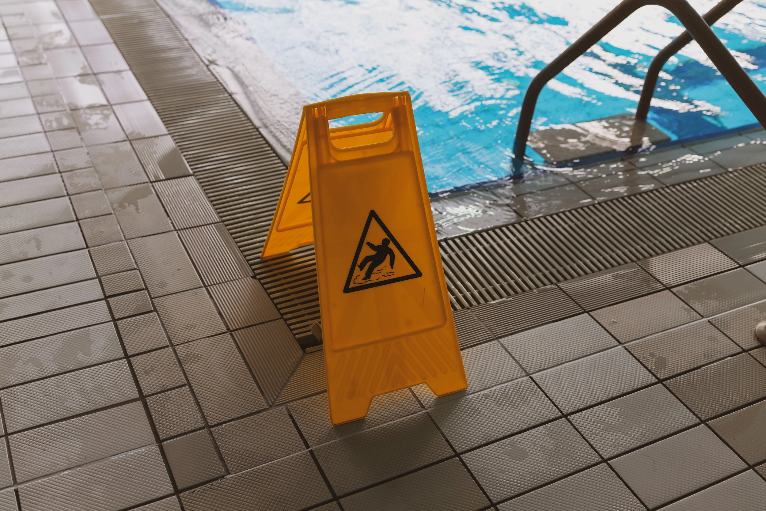 Orange wet floor caution sign on slippery wet tiles beside a swimming pool, a slip and fall hazard
