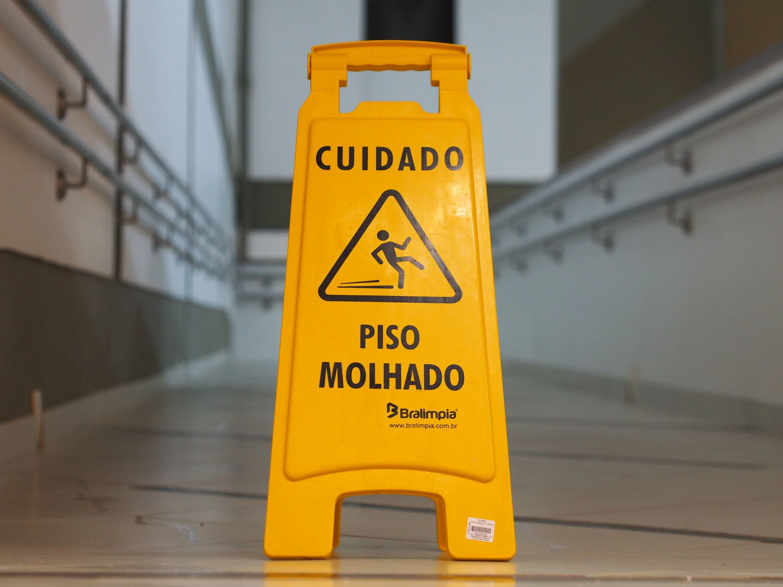 Yellow wet floor caution sign on a shiny floor near stairs, a slip and fall hazard on commercial property