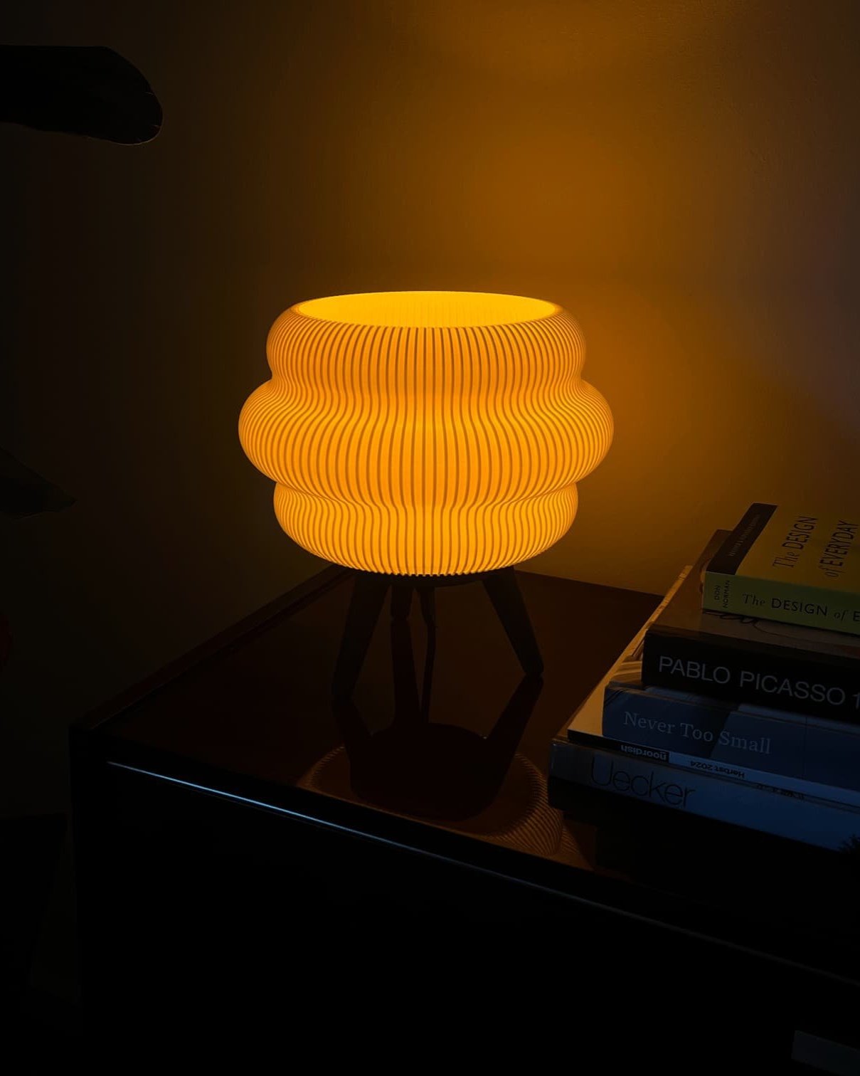 Kumo lamp placed on a bedside table, glowing with a candle-like warmth, enhancing a cozy reading nook.