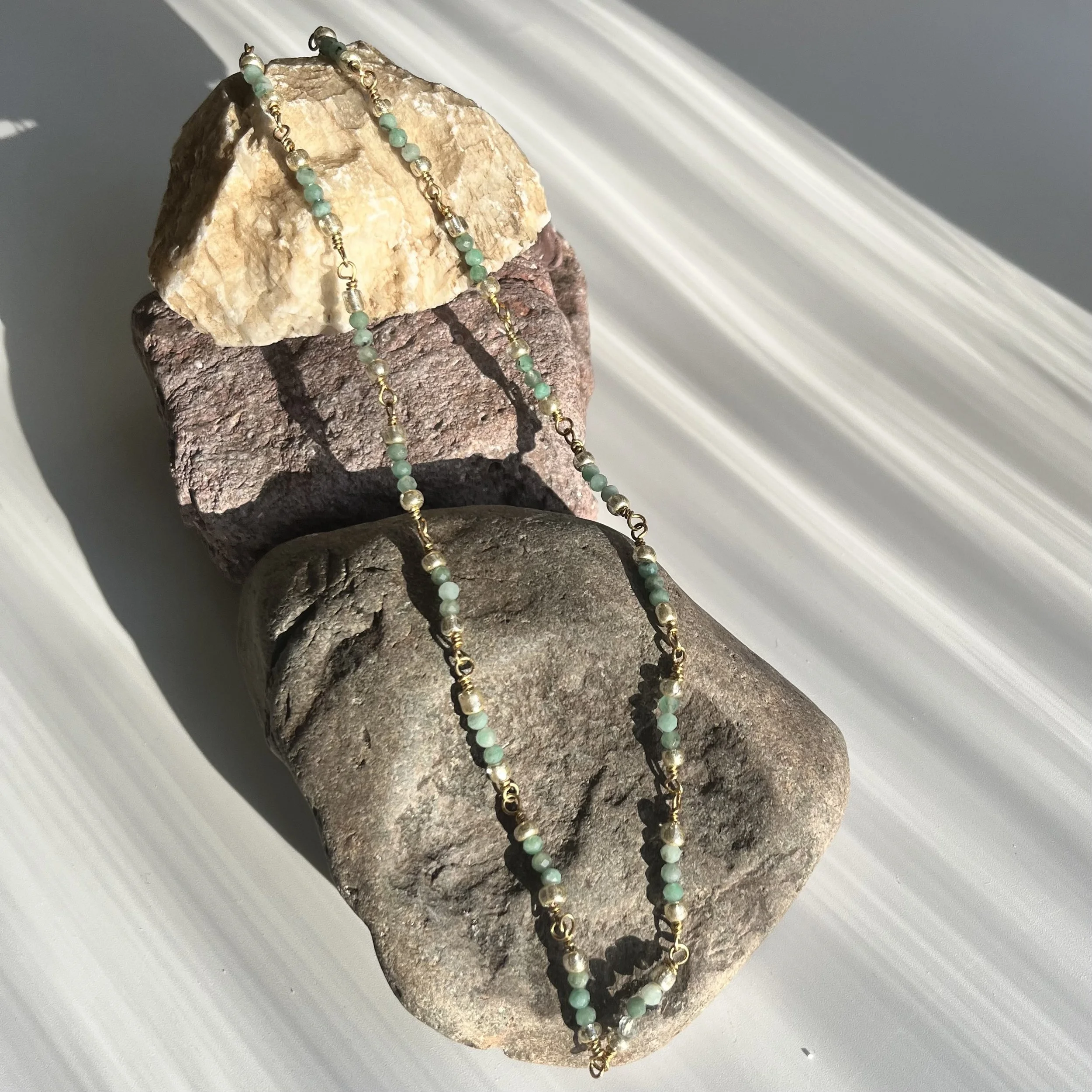 necklace of chained together 2mm emerald beads and Glass laying on a rock.