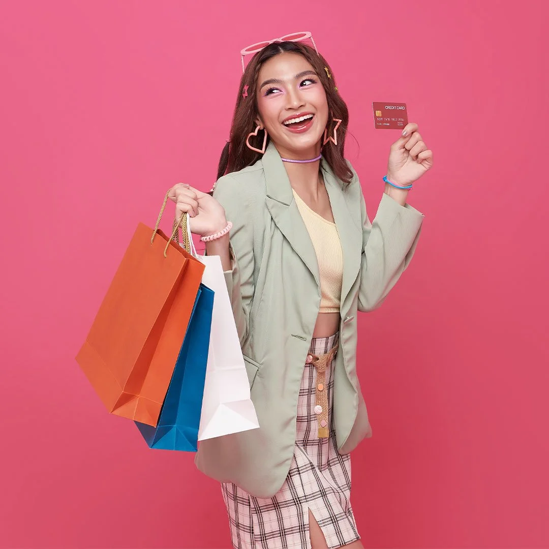 Person holding shopping bags and a credit card against a pink background