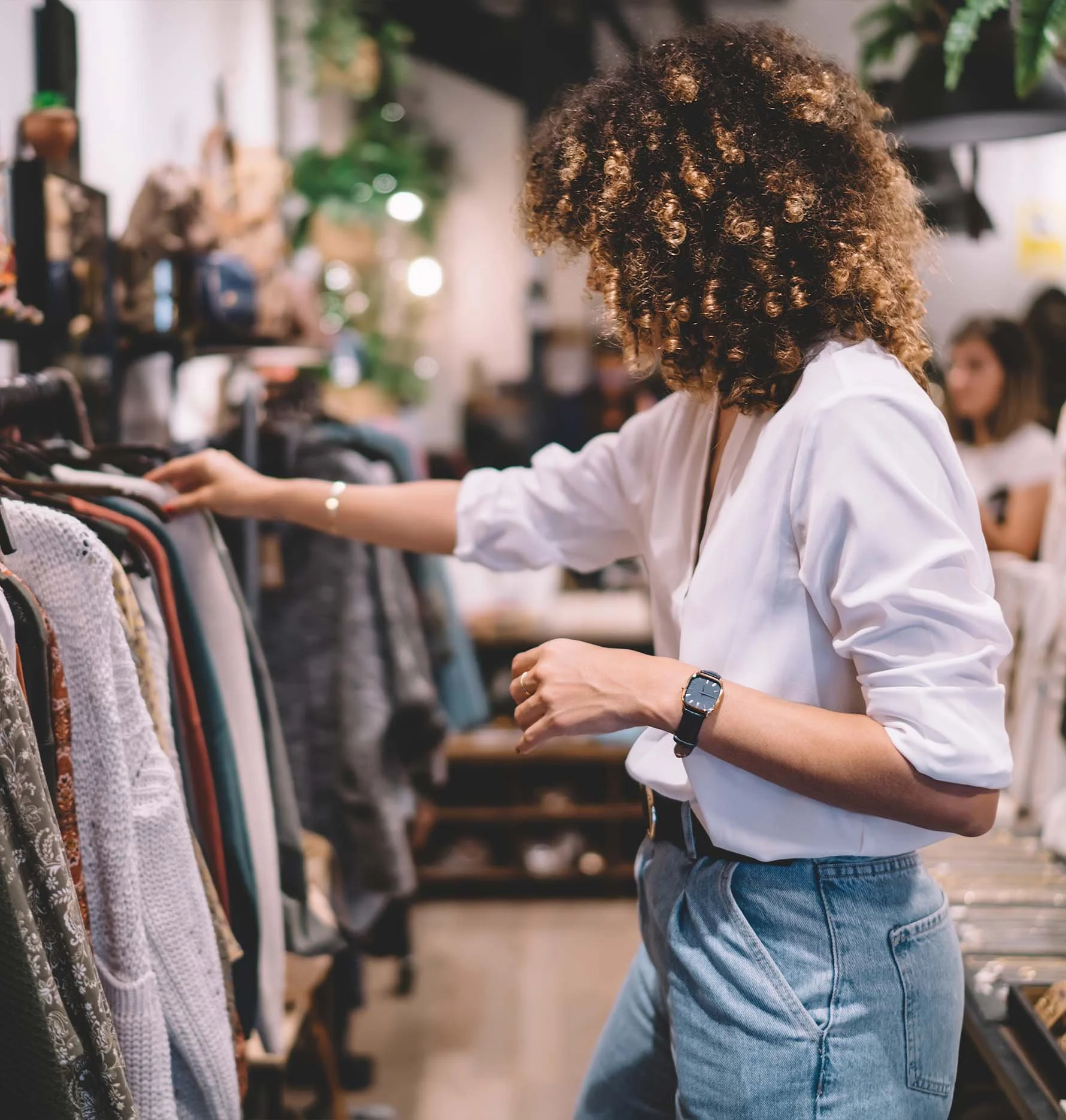 Person browsing clothes in a store, wearing a white shirt and jeans.