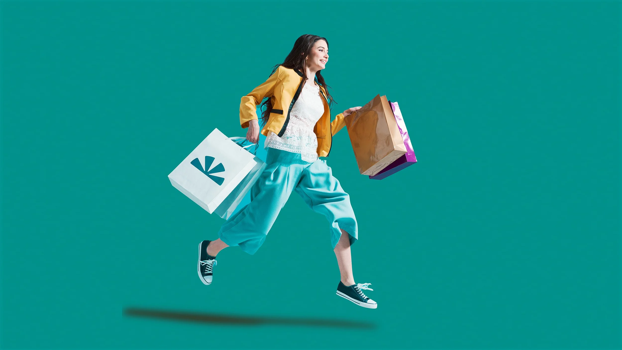 Woman shopping with bags jumping against teal background